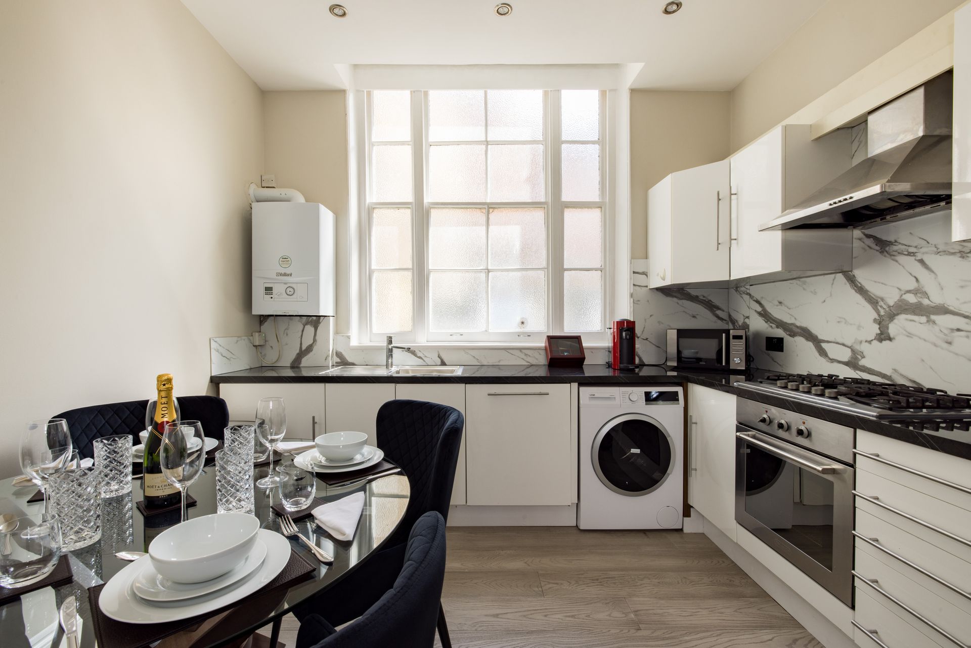 Modern white kitchen with dining table set, large window, and built-in appliances