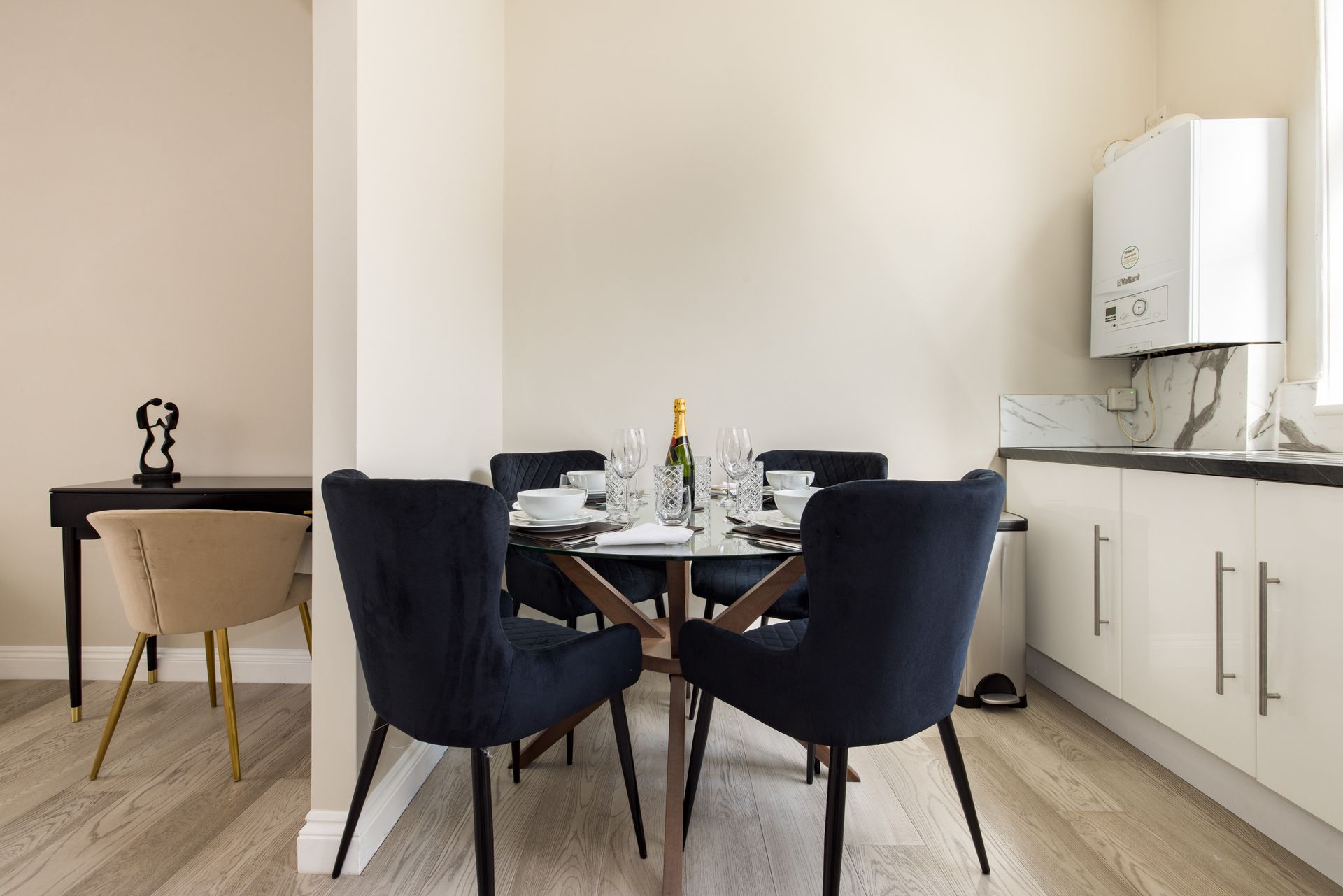 Modern dining area with black chairs, glass table, and white kitchen cabinets beside a marble countertop.