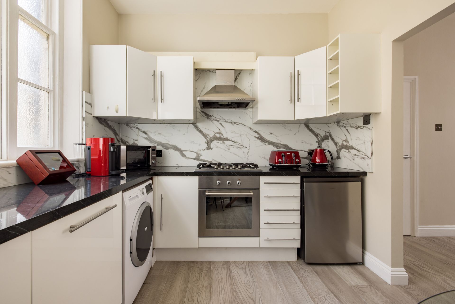Modern kitchen with white cabinets, black countertops, stainless appliances, and red toaster and kettle on the counter