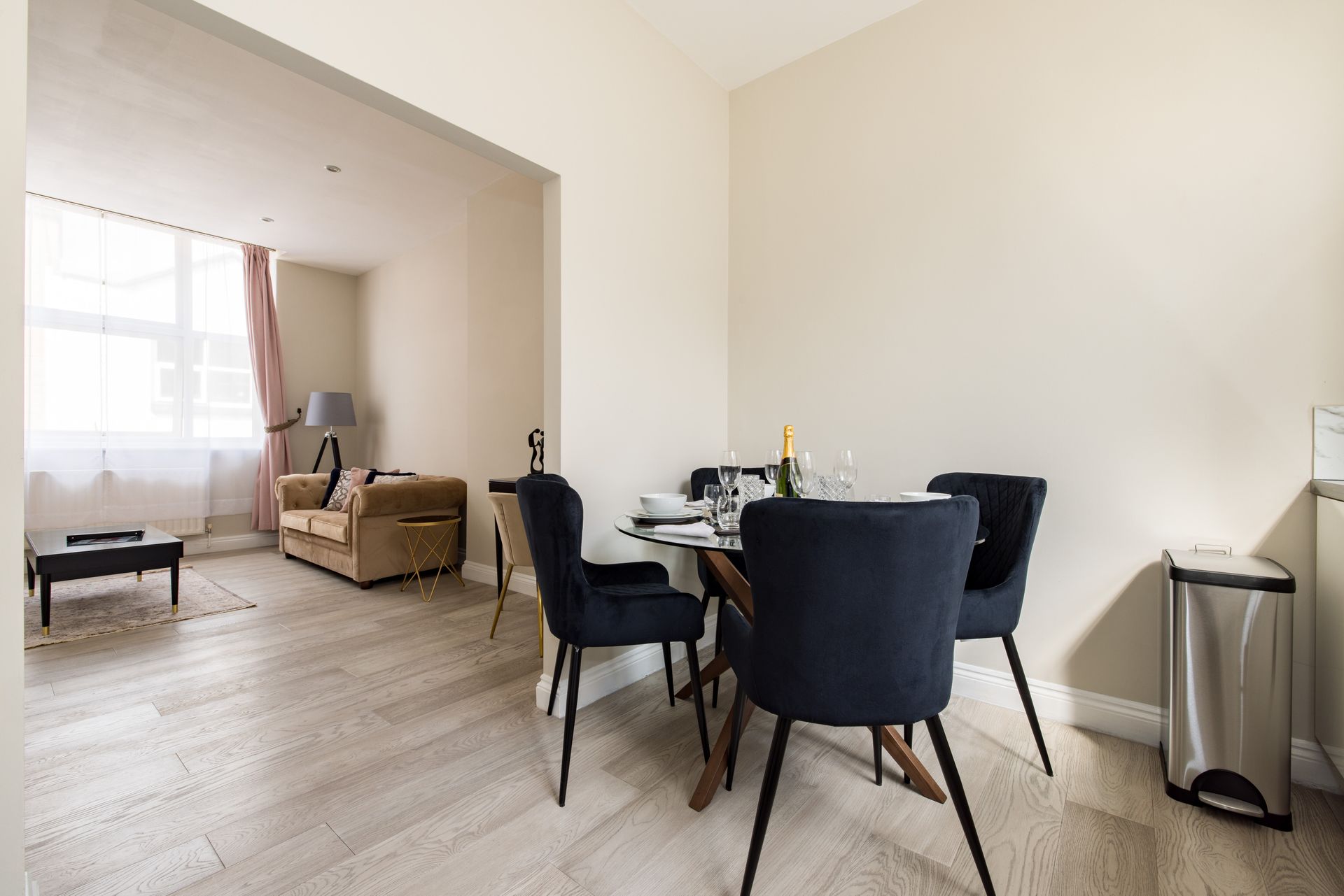Dining area with black chairs and a round table, opening into a bright living room with a sofa and window.
