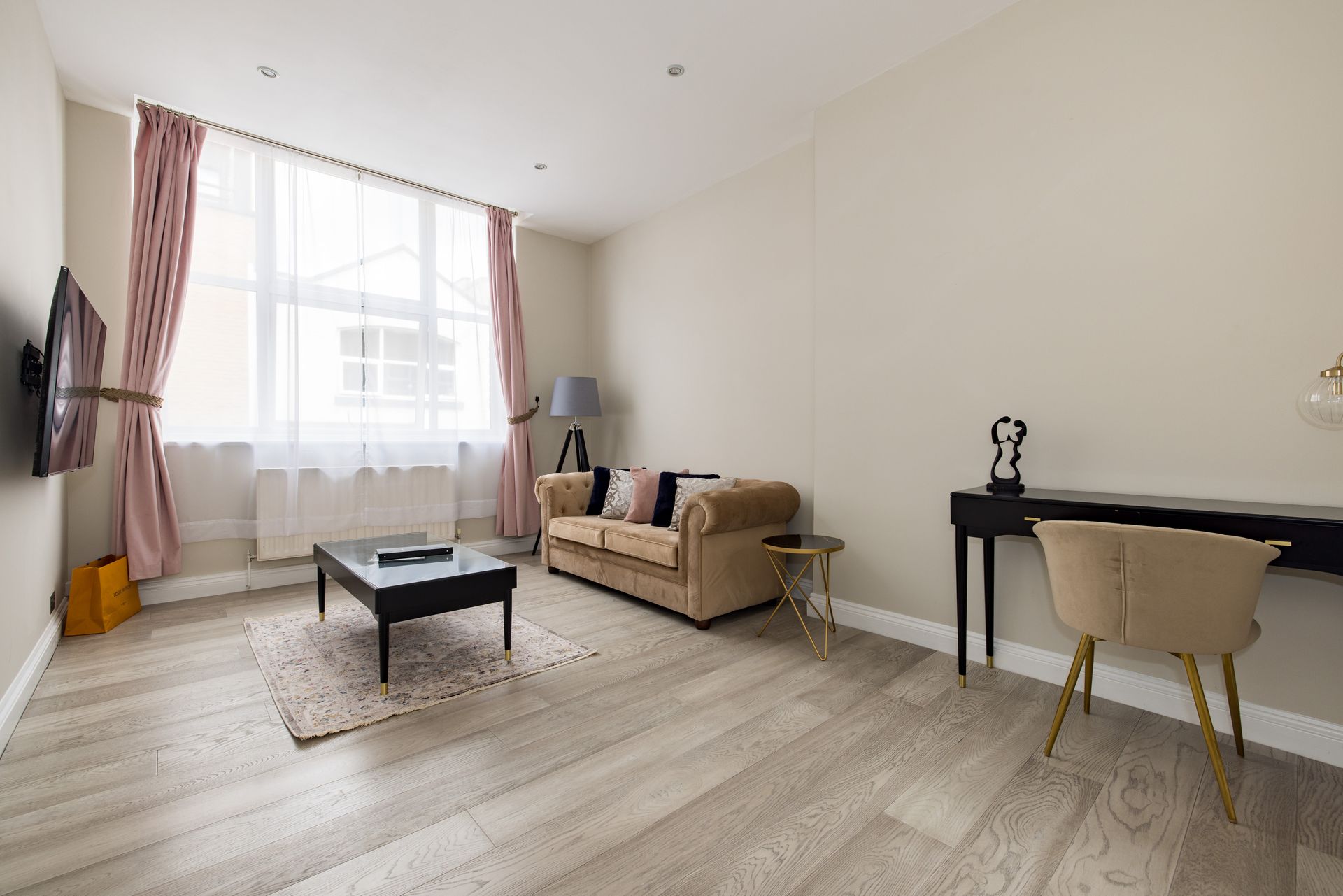Bright living room with sofa, coffee table, desk, and large window with pink curtains
