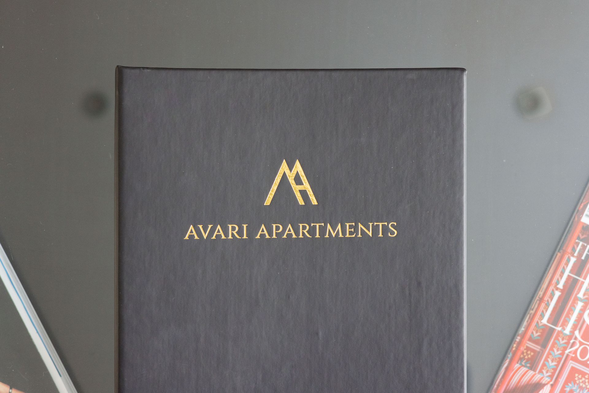 Black booklet with gold Avari Apartments logo on a gray surface