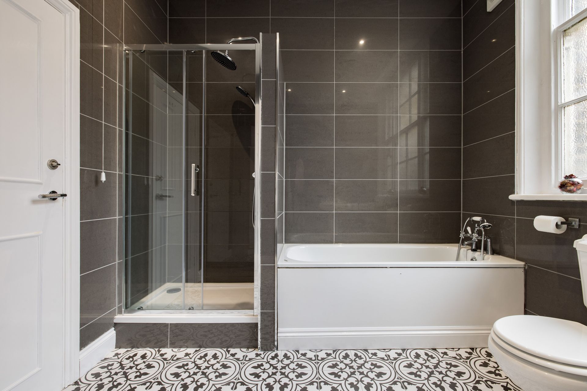 Modern bathroom with glass shower, white tub, and patterned tile floor