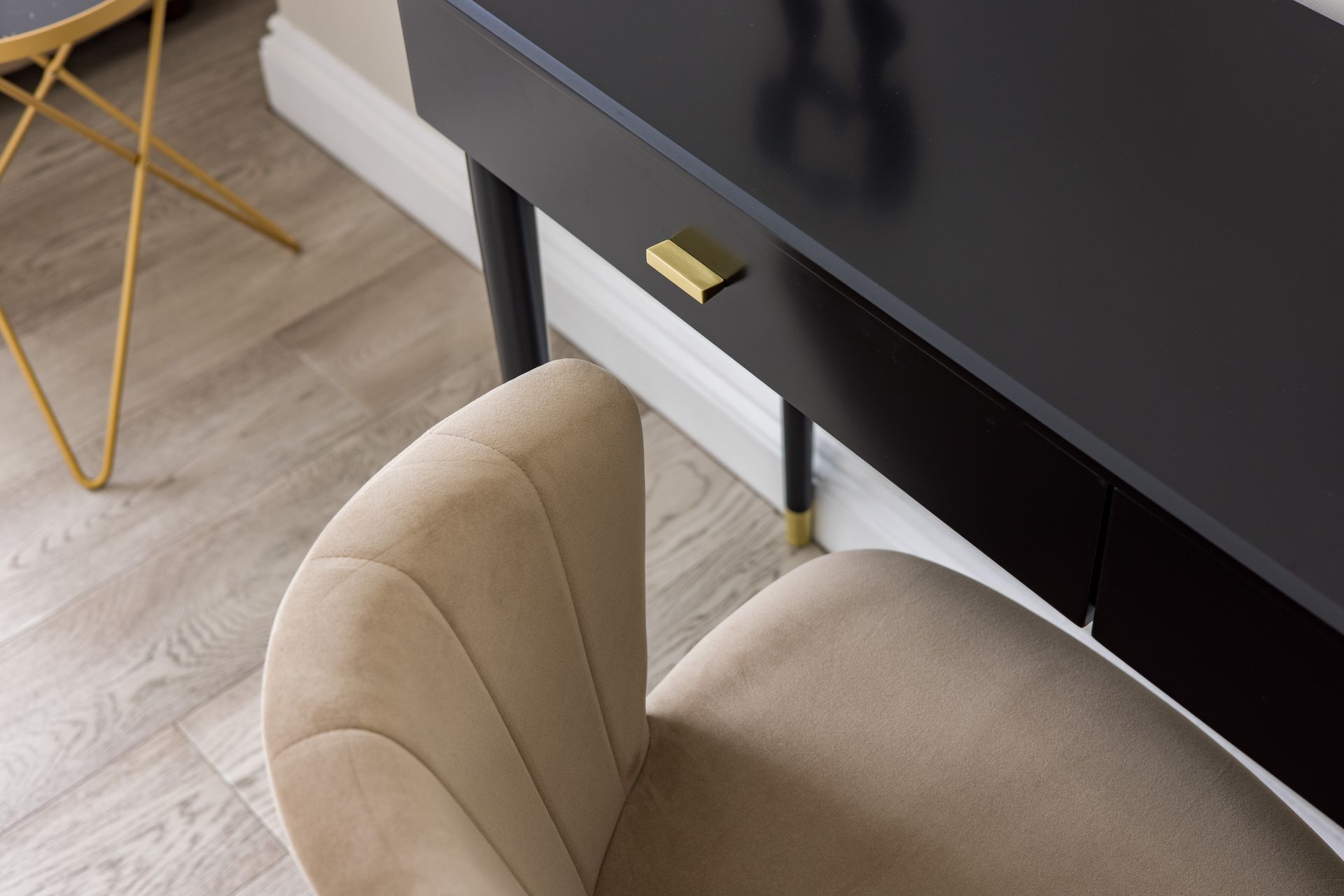 Beige chair beside a black desk with a gold handle on a light wood floor.
