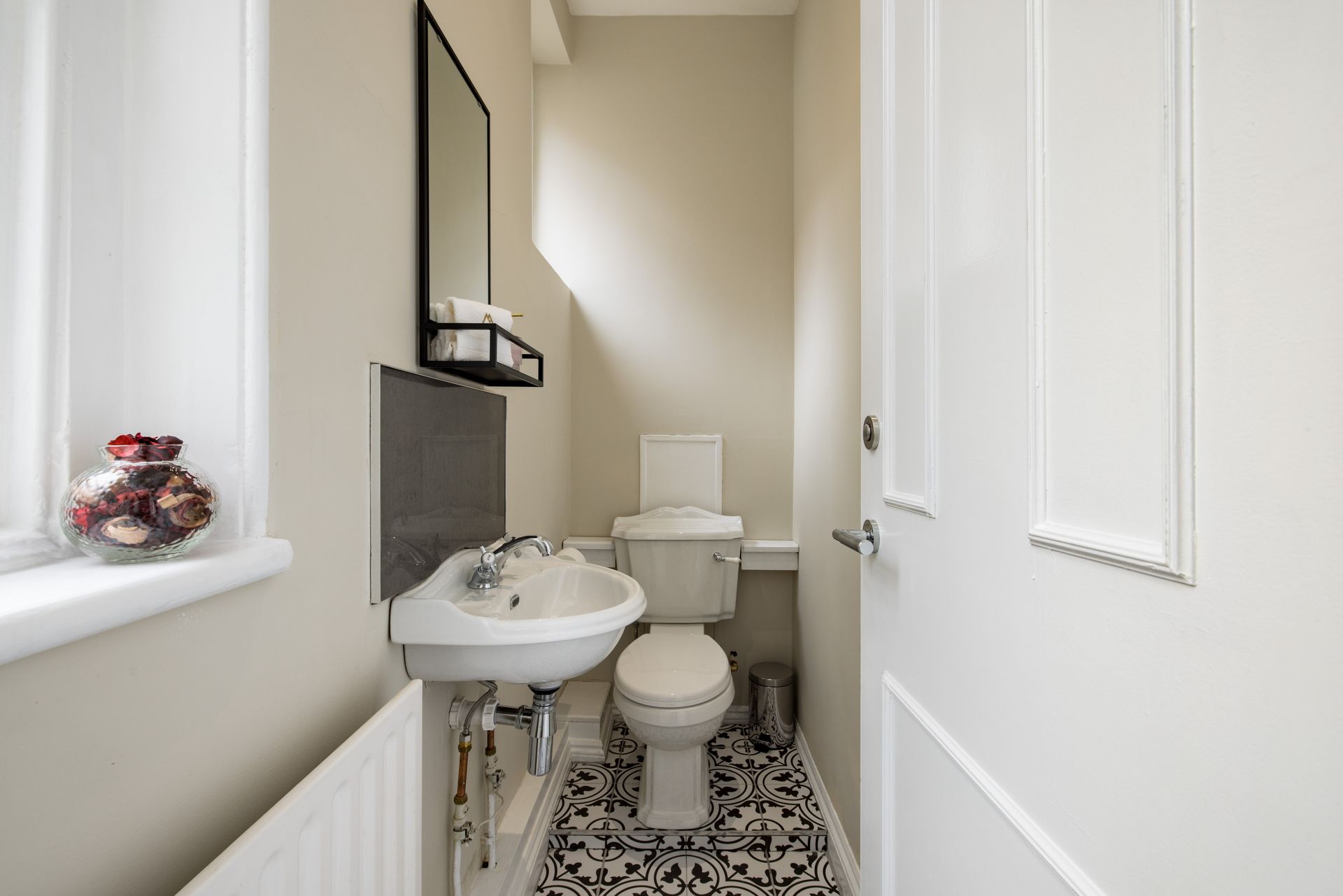 Narrow bathroom with sink, toilet, and patterned floor tiles, seen from the doorway.