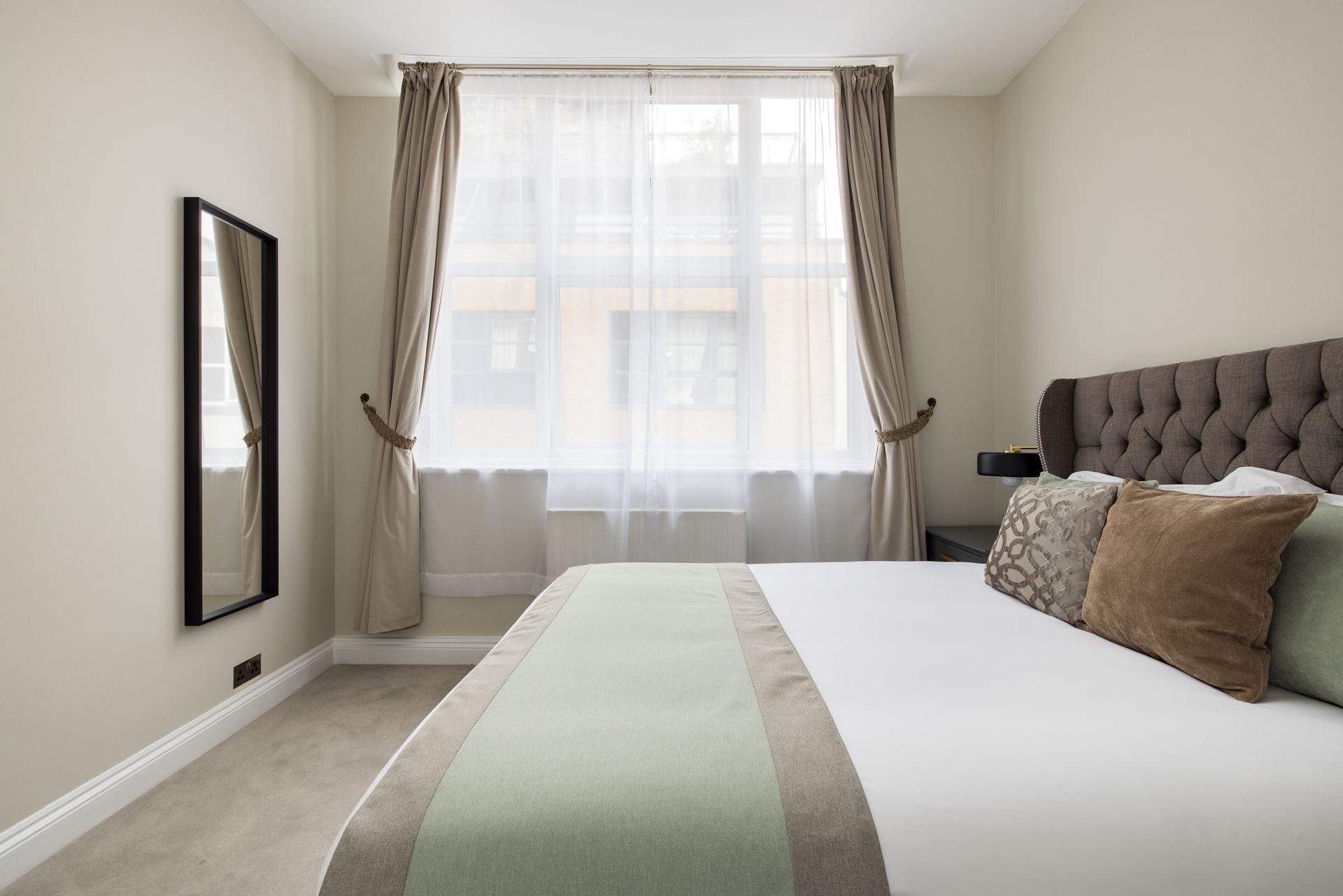 Bright bedroom with a large bed, tufted headboard, and window with curtains