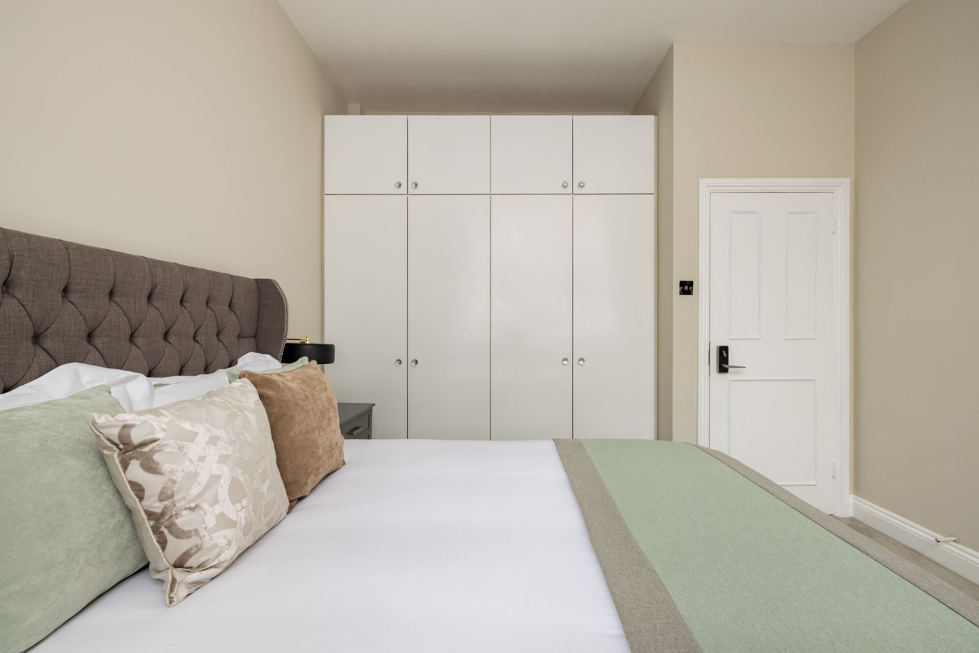 Bright bedroom with a tufted headboard, white bedspread, and built-in white closet doors.
