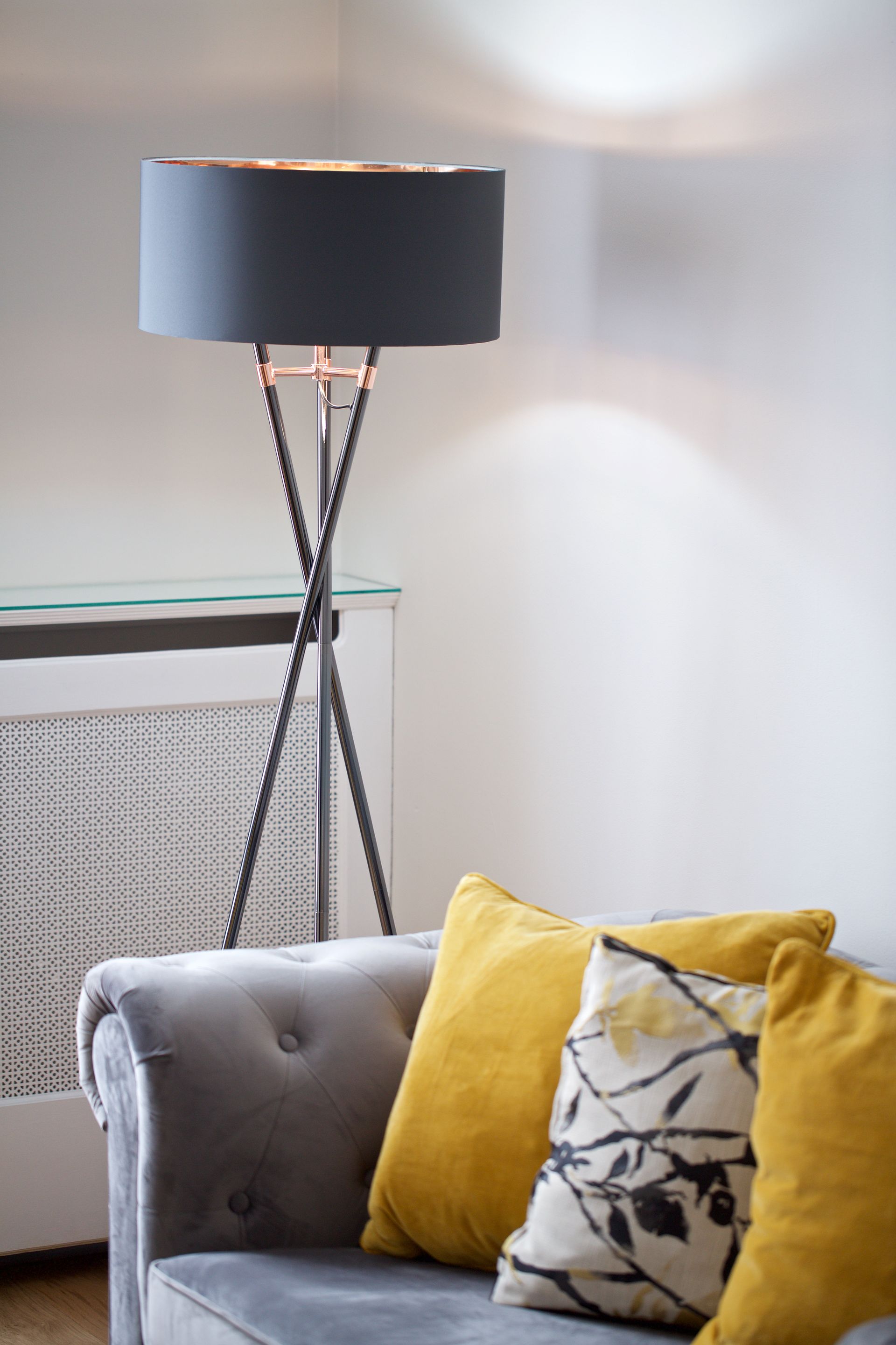 Modern living room corner with a gray sofa, yellow pillows, and a black floor lamp beside a radiator.
