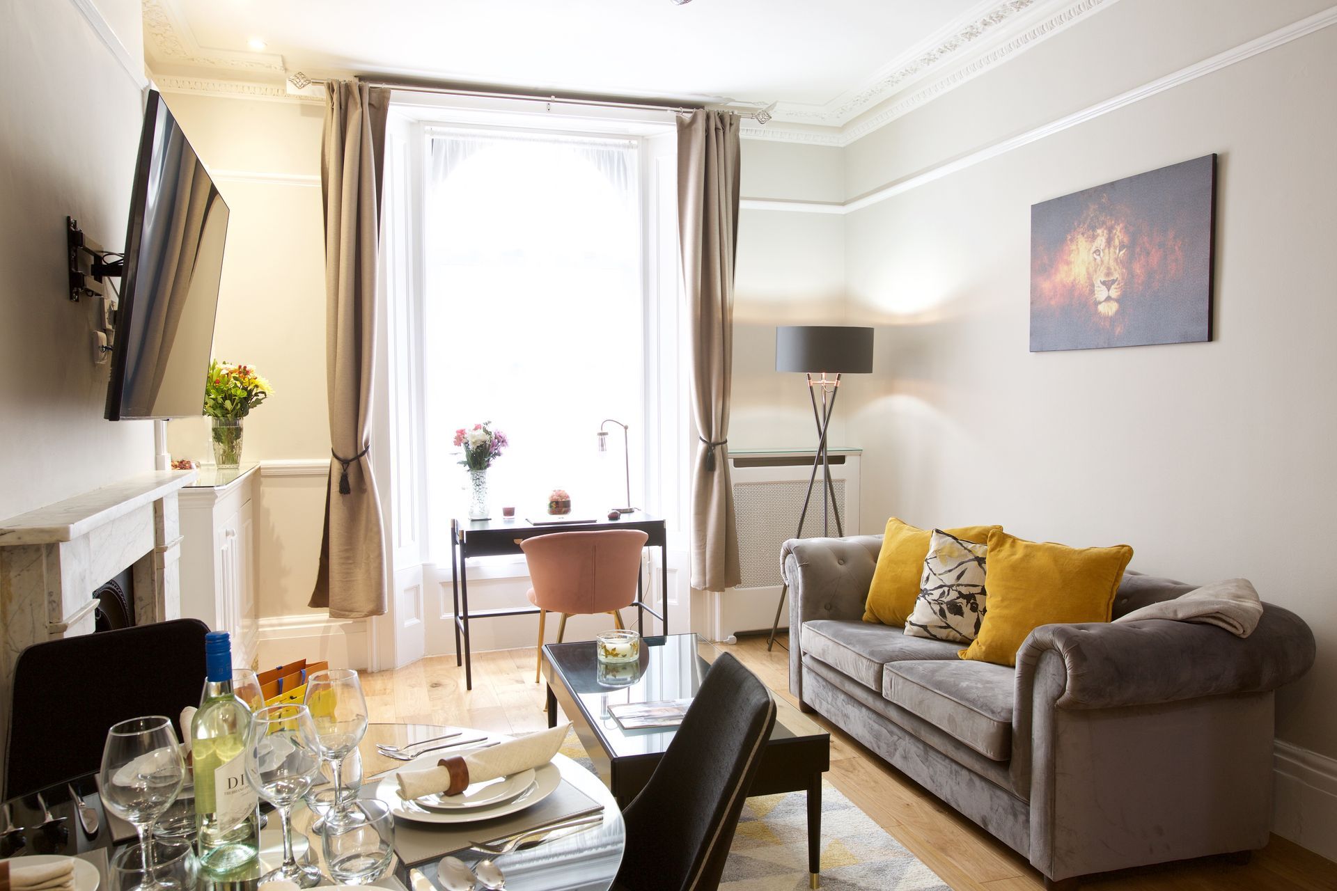 Bright living room with sofa, glass dining table, floor lamp, and sunlit window with curtains