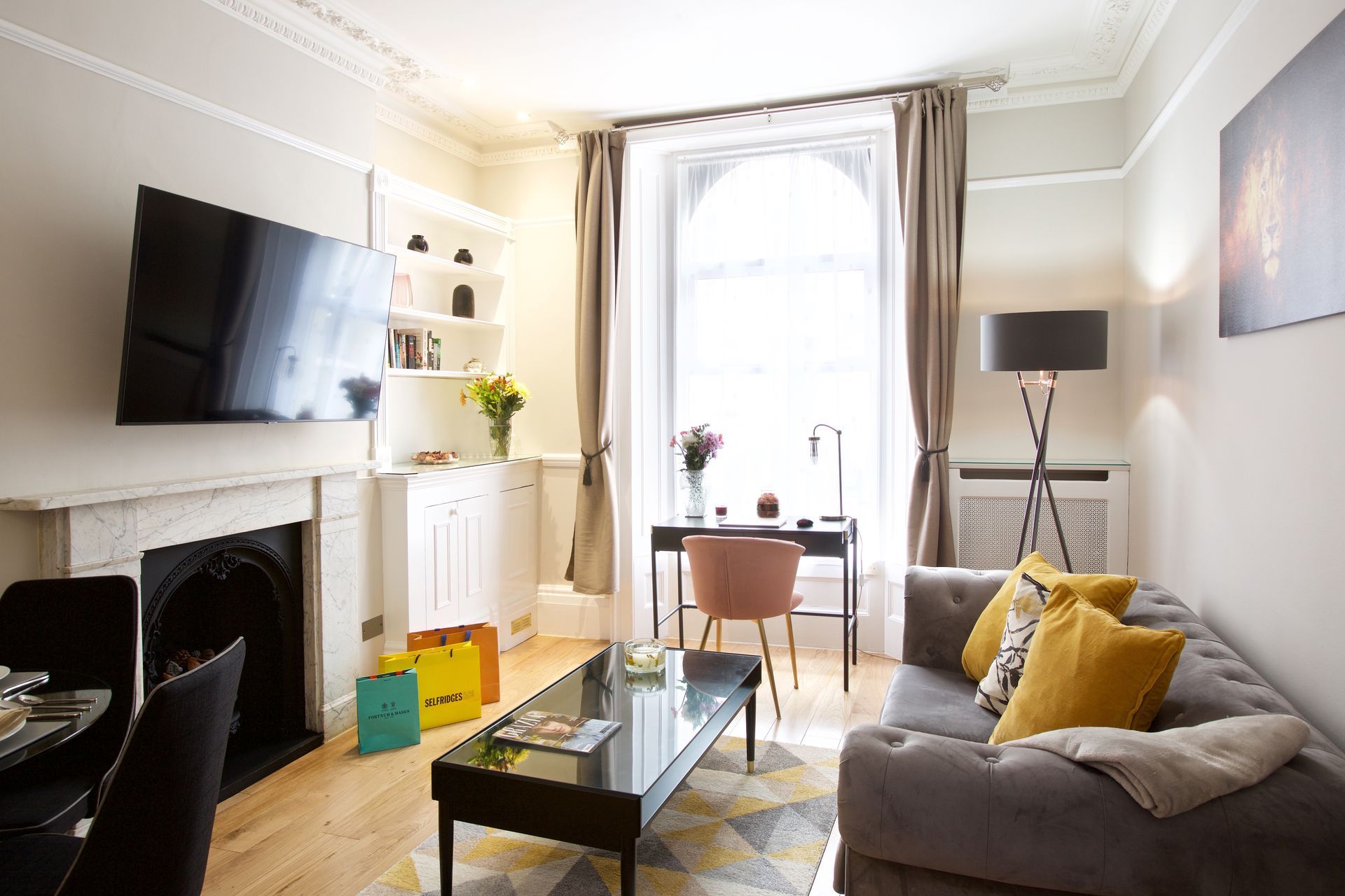 Bright living room with gray sofa, wall-mounted TV, fireplace, glass coffee table, and large window seating area