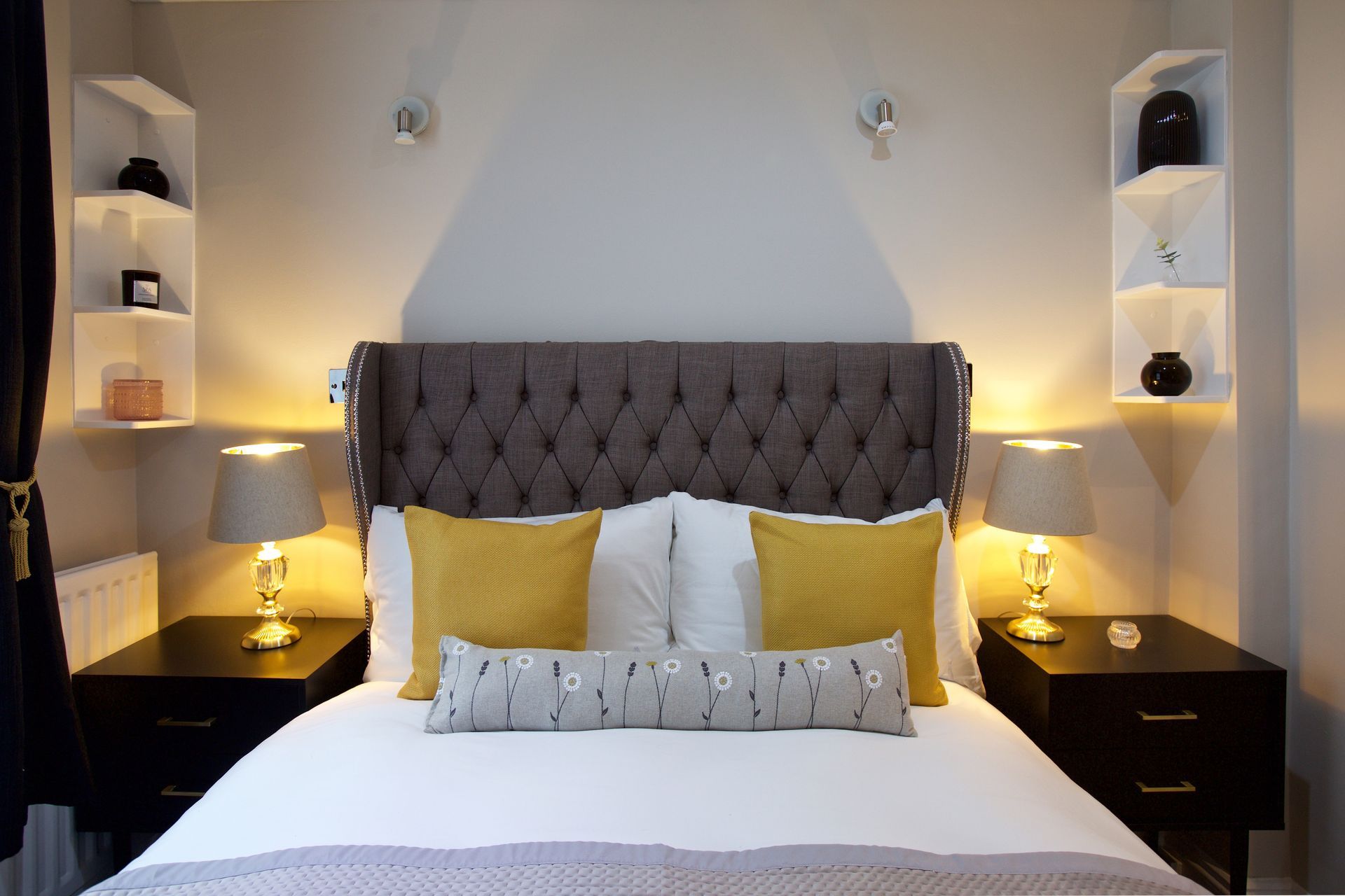 Modern bedroom with a tufted gray headboard, white bedding, yellow accents, and bedside lamps