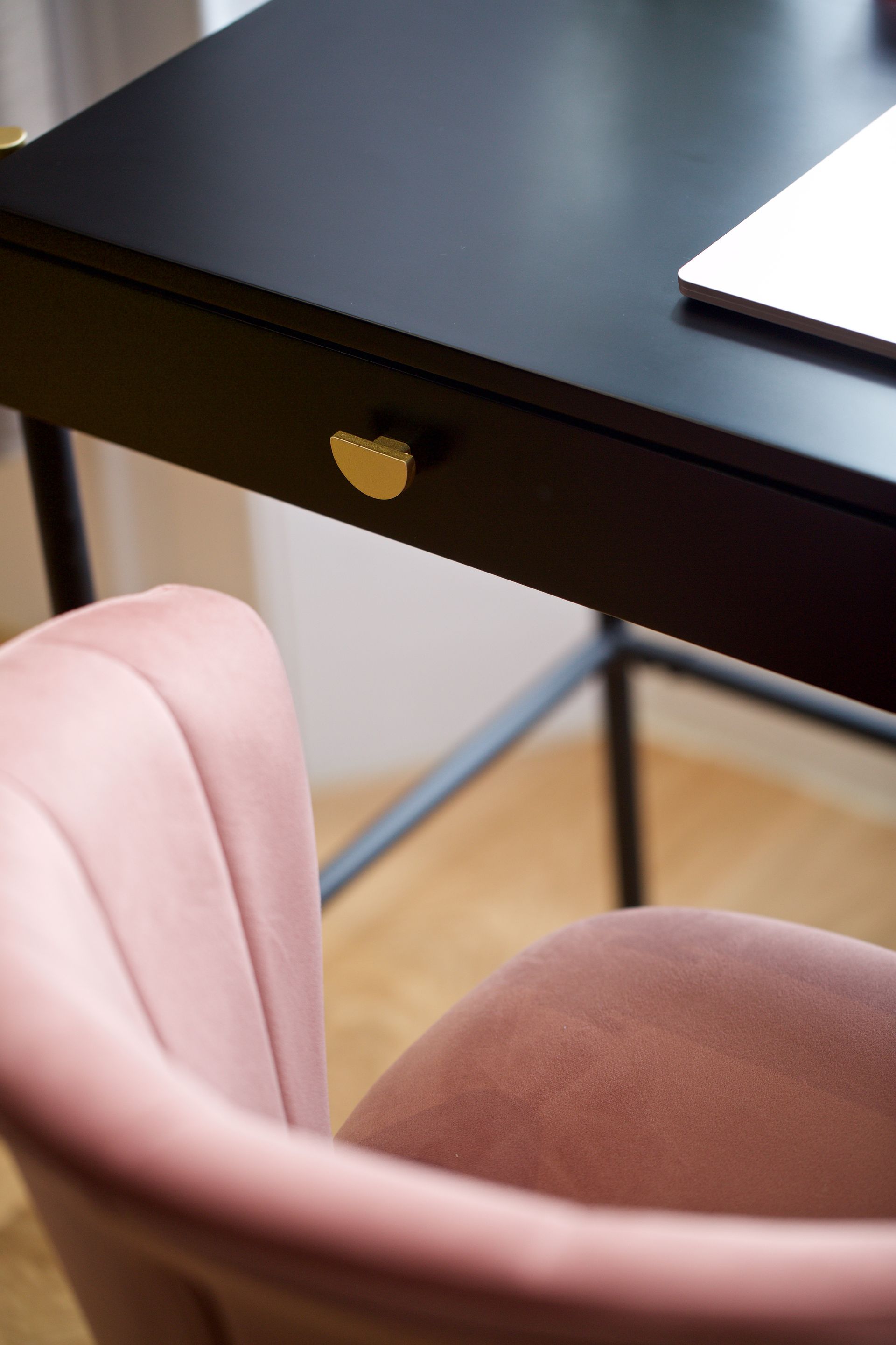 Black table edge above pink upholstered chair in a room with wood floor