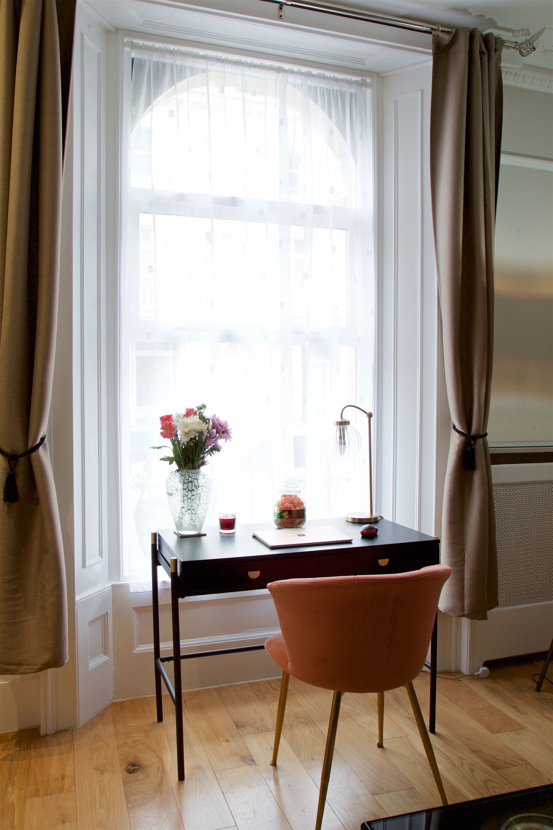 Small desk by a bright window with flowers, a candle, and an orange chair in a cozy room