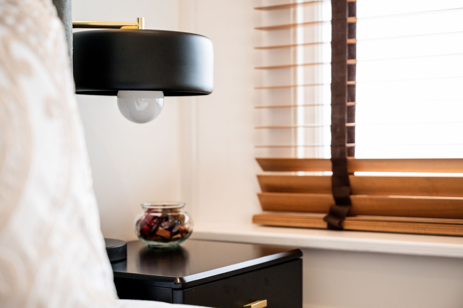 Bedroom corner with black lamp, bedside table, jar of candy, and window blinds