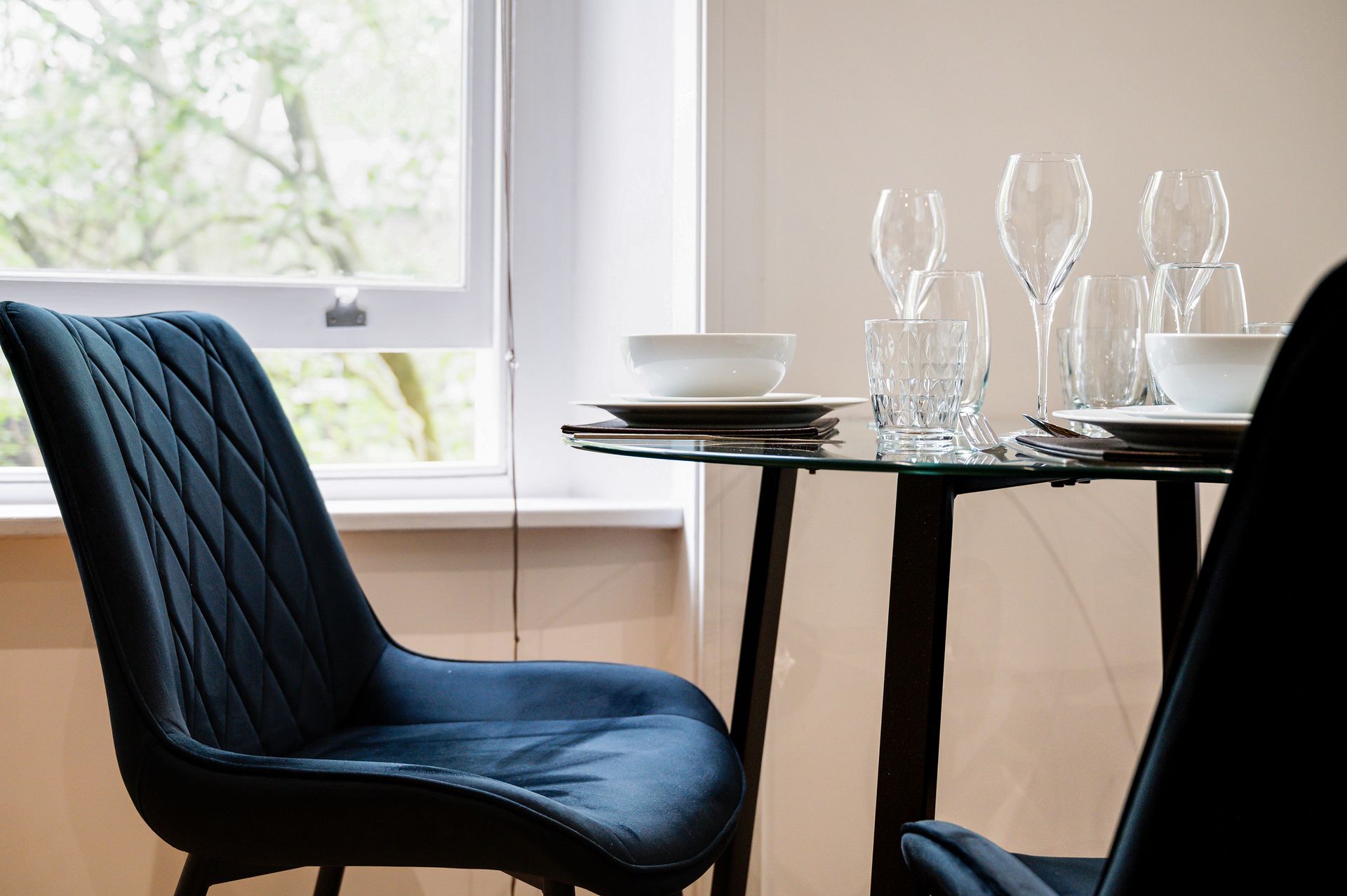Blue dining chair by a window beside a set table with glassware and plates