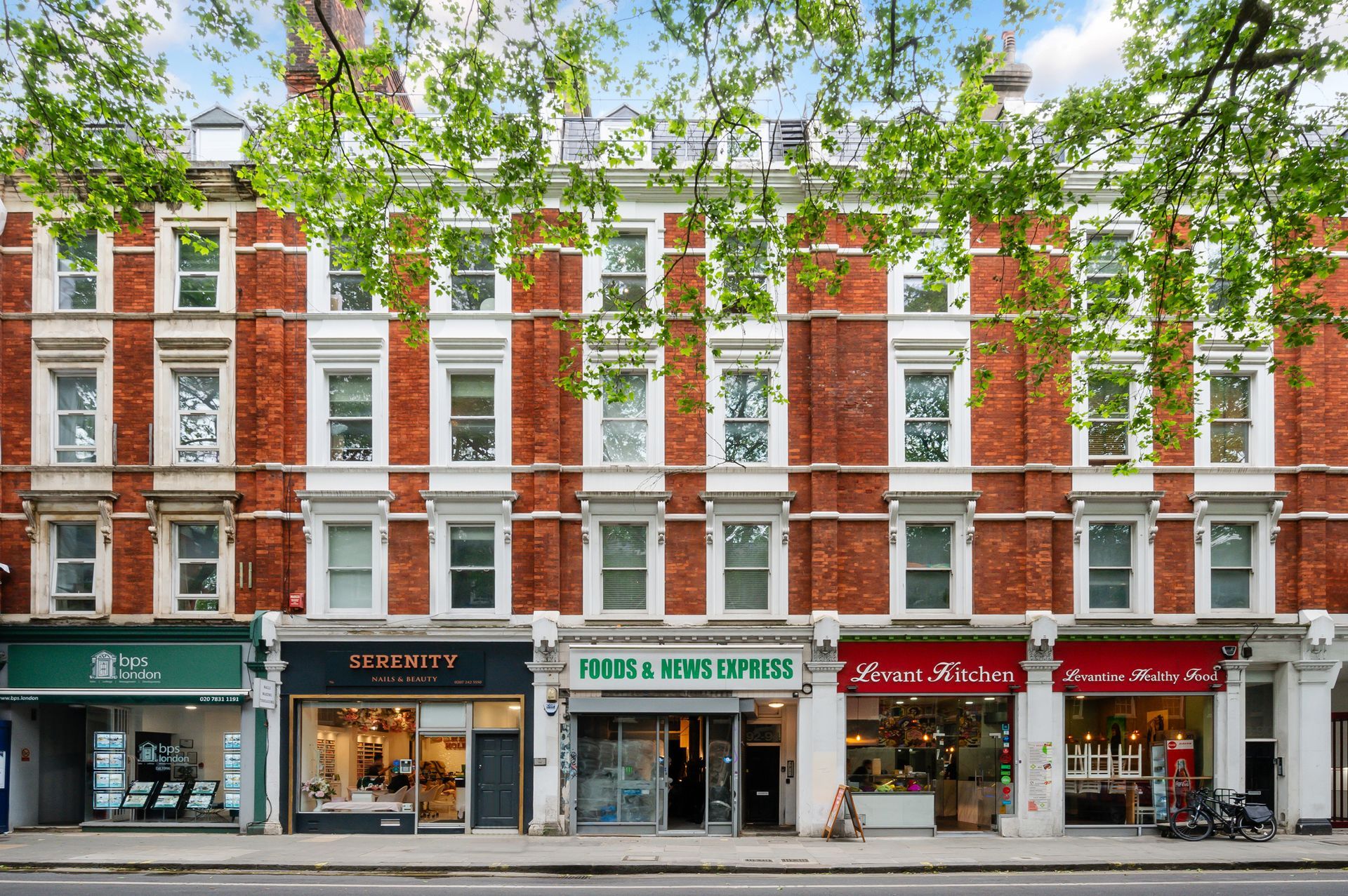 Red-brick row of shops with white windows and green trees along a city street