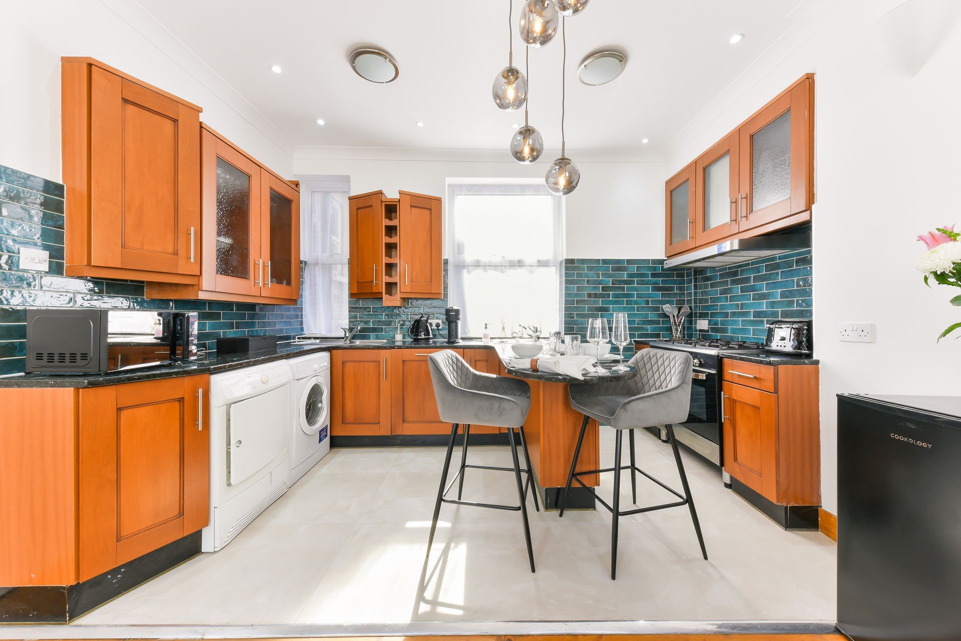 Bright modern kitchen with orange cabinets, blue tile backsplash, and a small dining table.