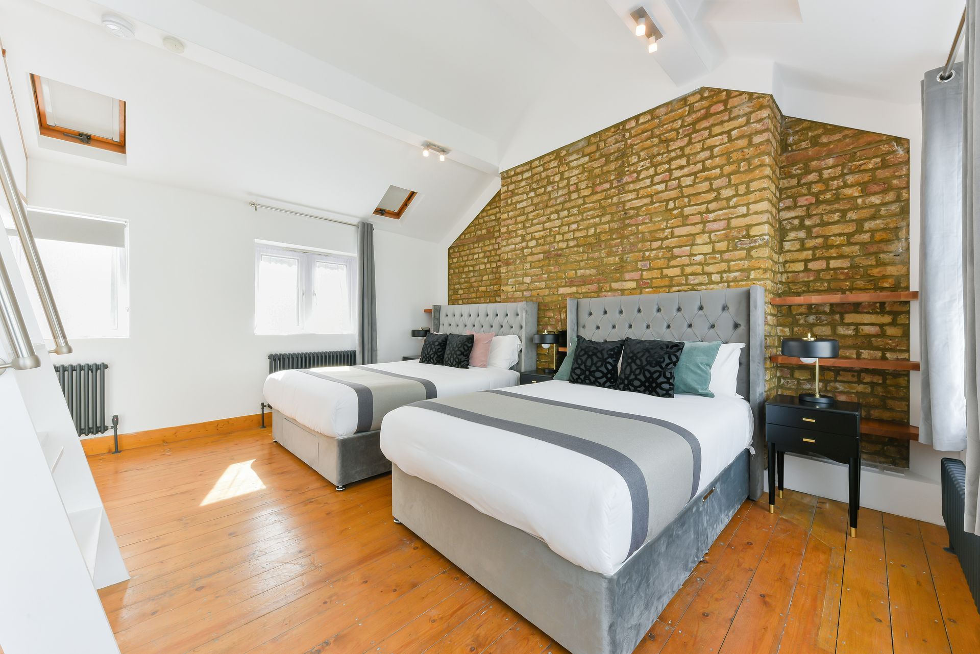 Bright loft bedroom with two twin beds, exposed brick wall, white walls, and wooden floors