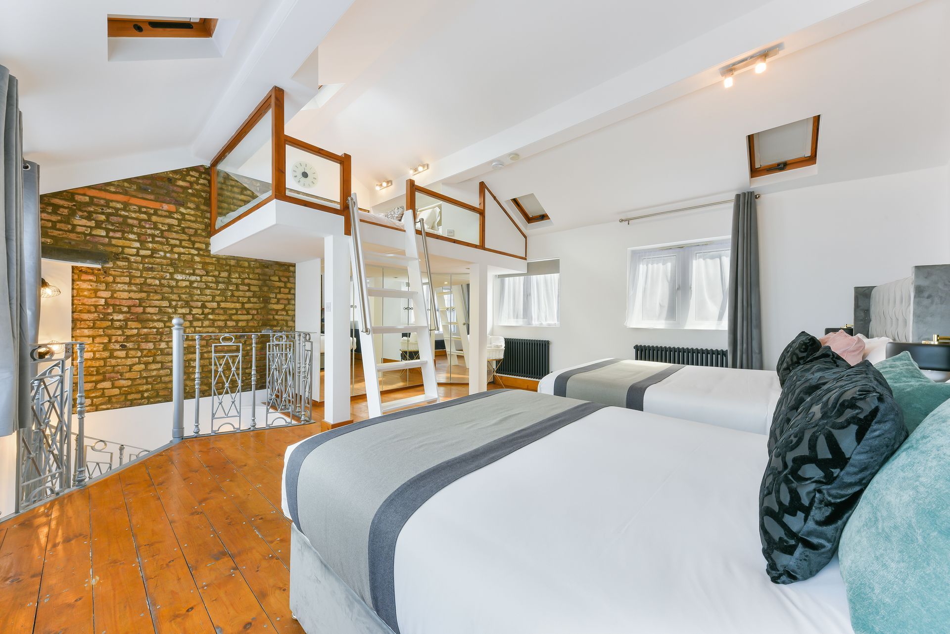 Bright loft bedroom with two beds, exposed brick wall, white walls, and wooden floor