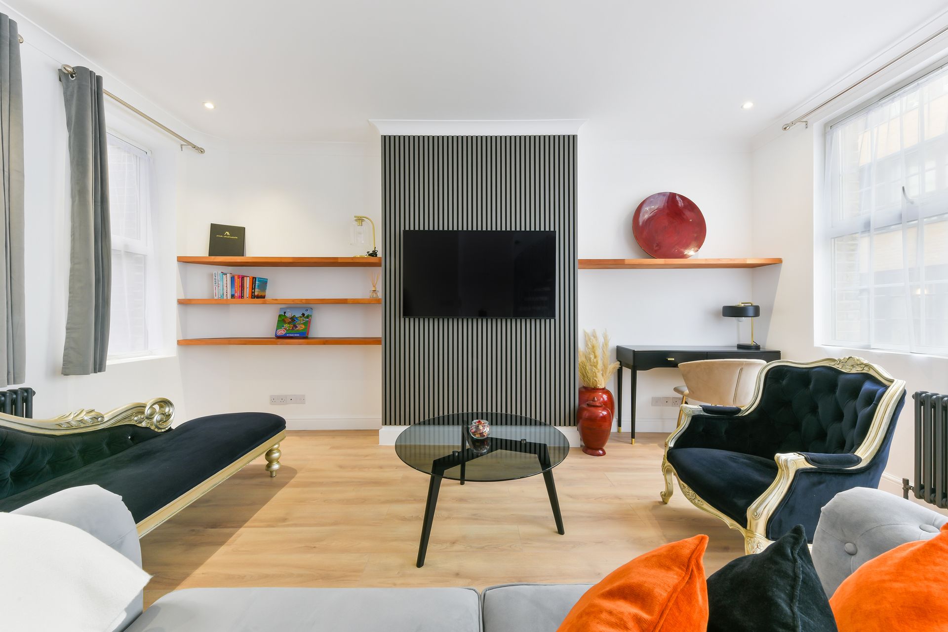 Bright modern living room with striped TV wall, black sofas, and orange accents