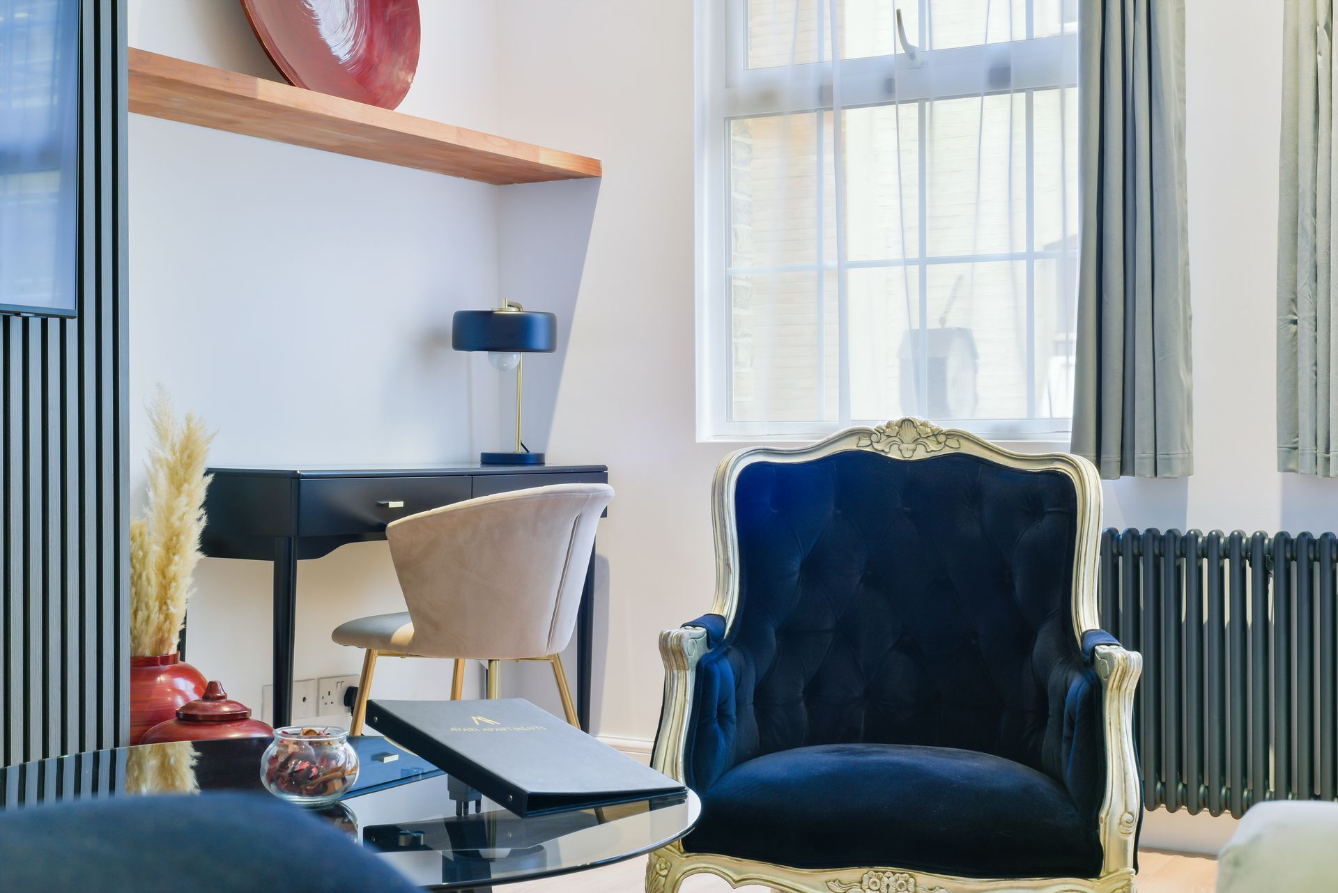 Modern living room with blue velvet chair, white desk, window light, and pale walls