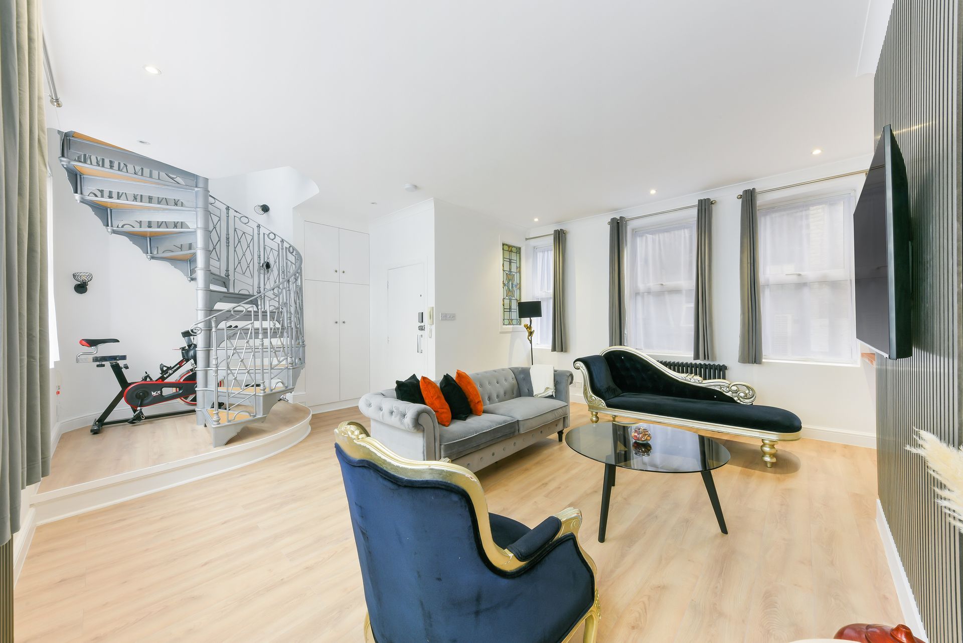 Bright modern living room with spiral staircase, gray sofa, blue chair, and large windows
