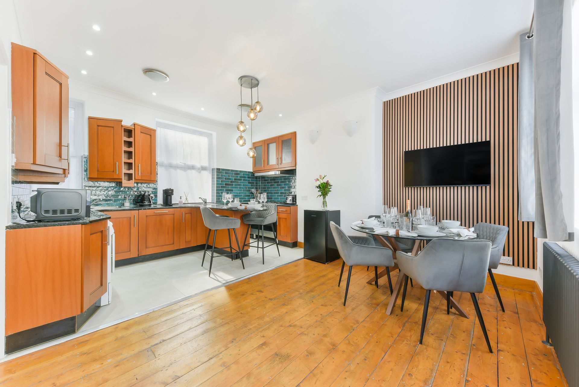 Bright modern open-plan kitchen and dining area with wood floors, orange cabinets, and a wall-mounted TV.