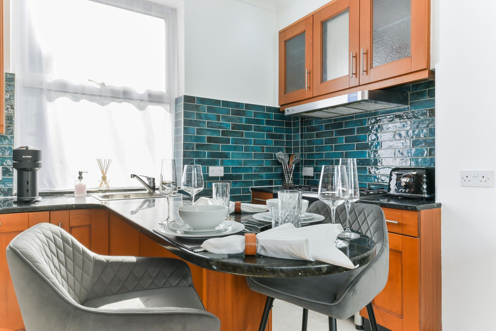Modern kitchen with orange cabinets, teal tile backsplash, and a small dining table set for two