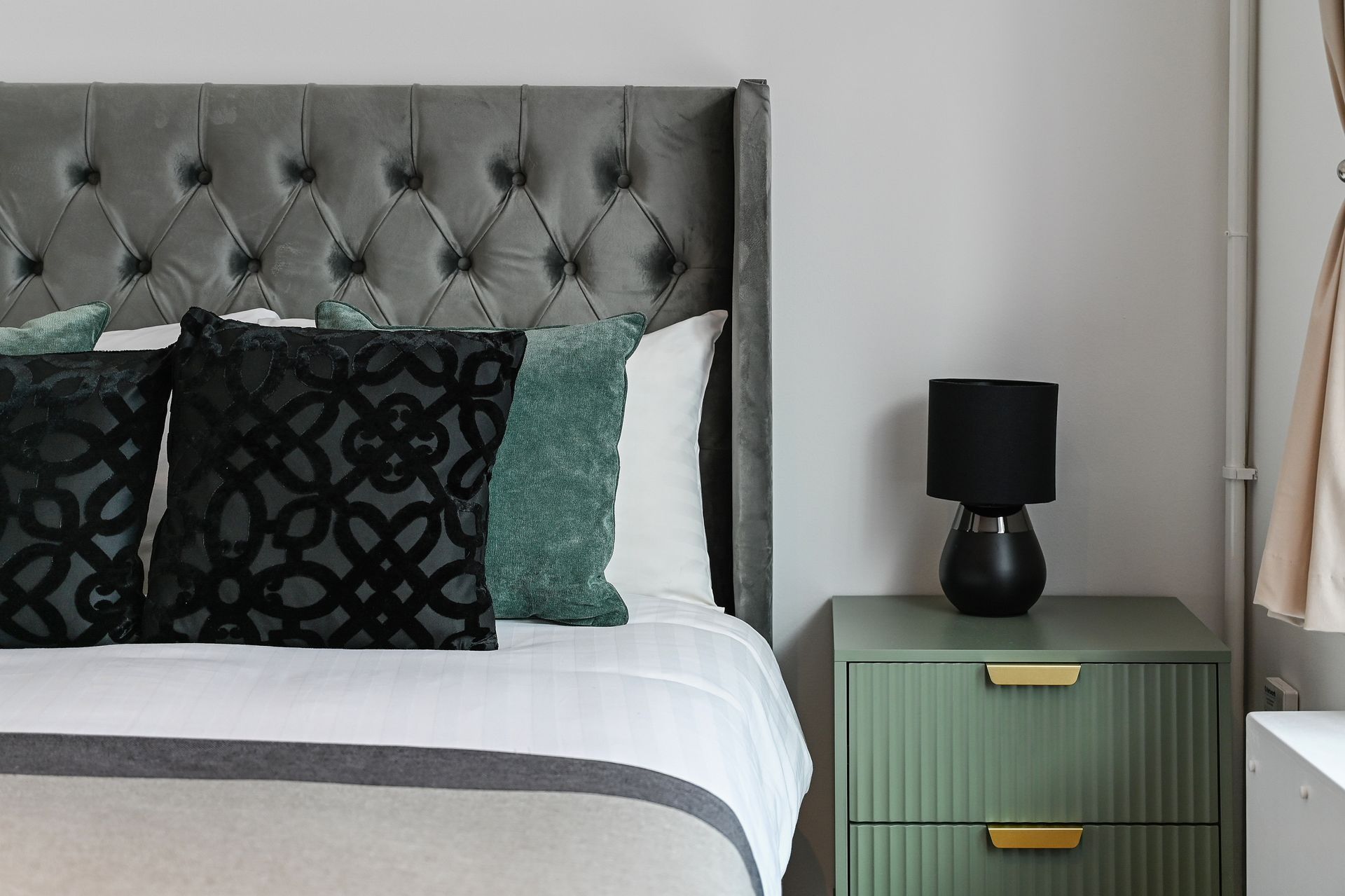 Tufted gray headboard with bed, patterned pillows, and mint green nightstand with black lamp