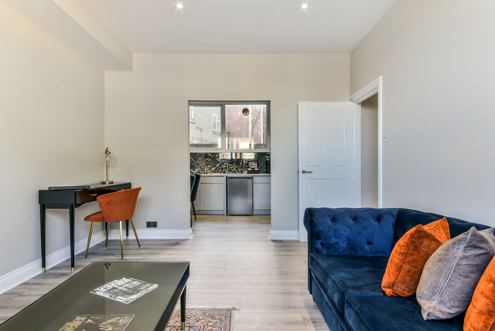 Bright living room with navy sofa, desk, and open view to a kitchen area and balcony door