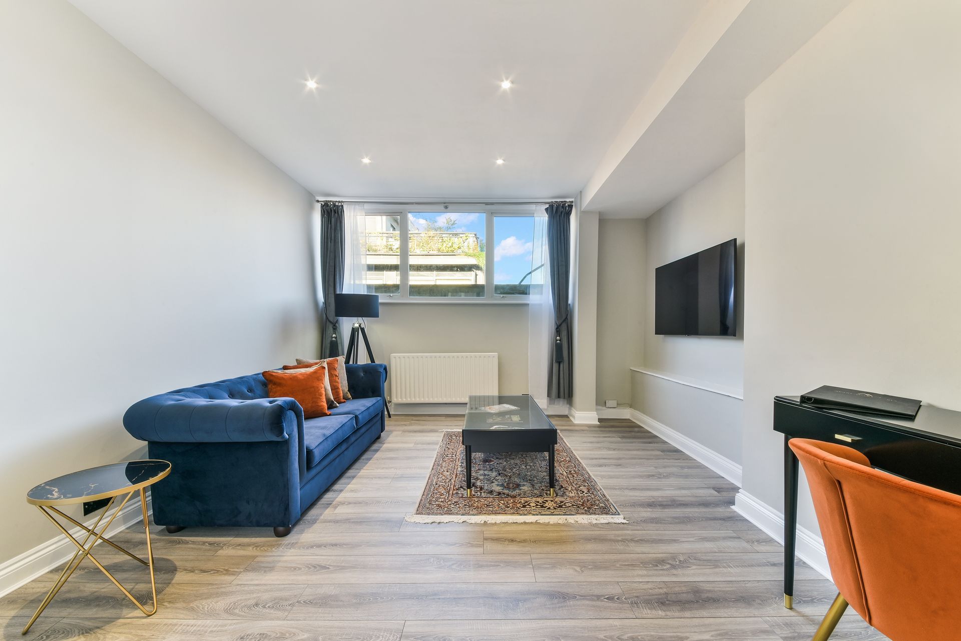 Modern living room with blue sofa, orange chair, wall-mounted TV, and coffee table by a window