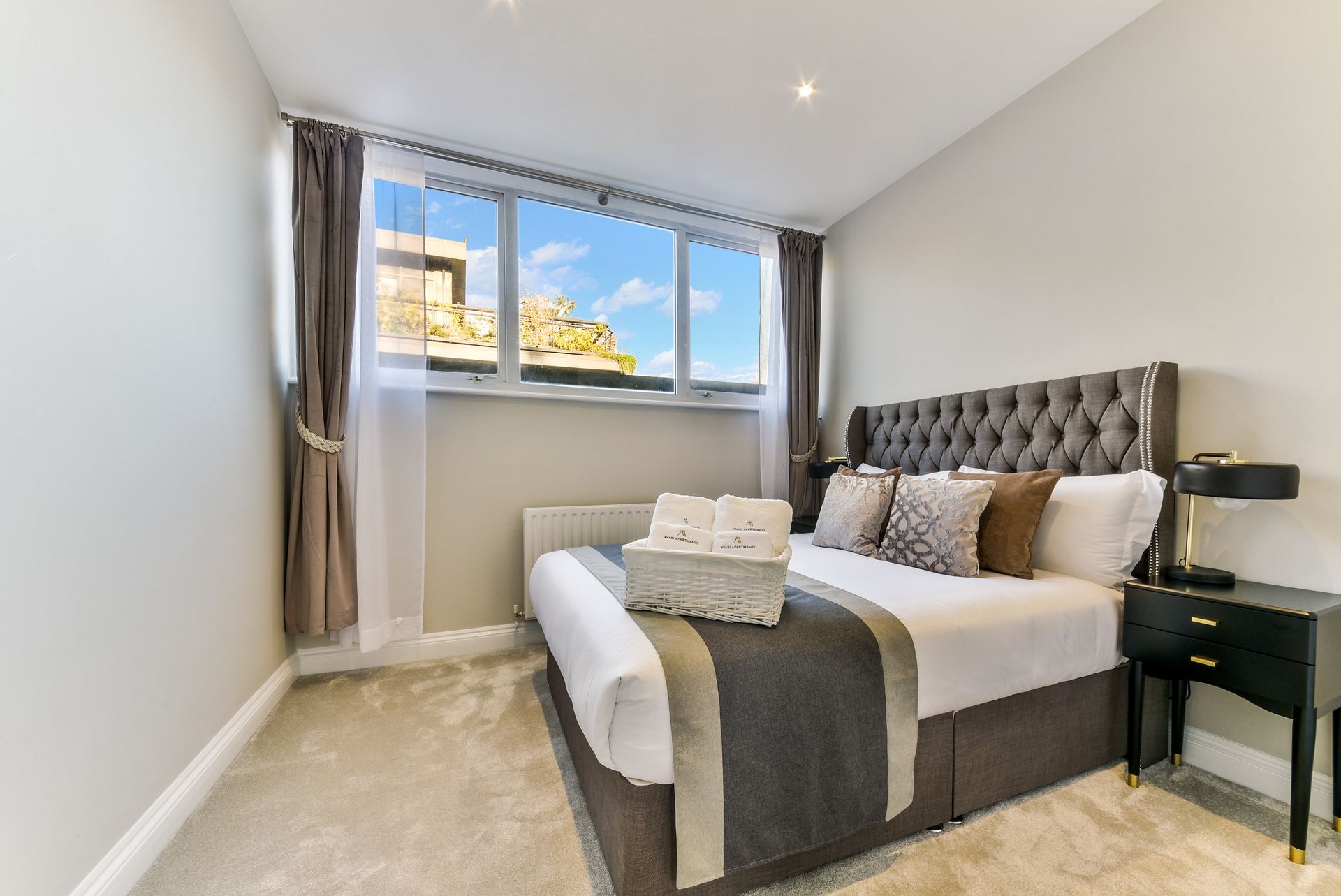 Bright bedroom with a tufted bed, gray curtains, and a large window letting in natural light.