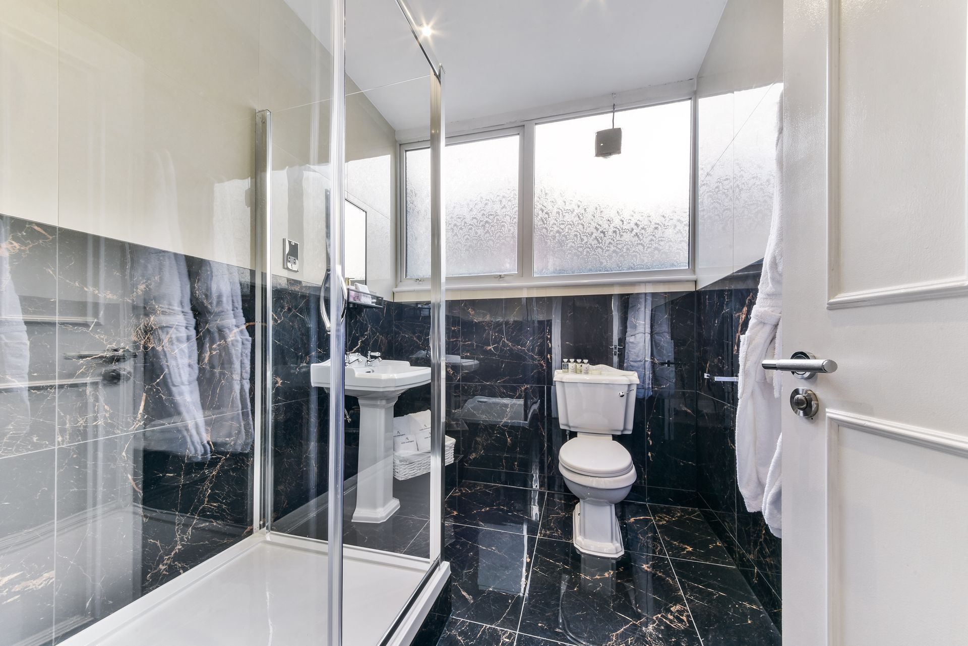Small bathroom with a glass shower, toilet, sink, and black-and-white tiled walls