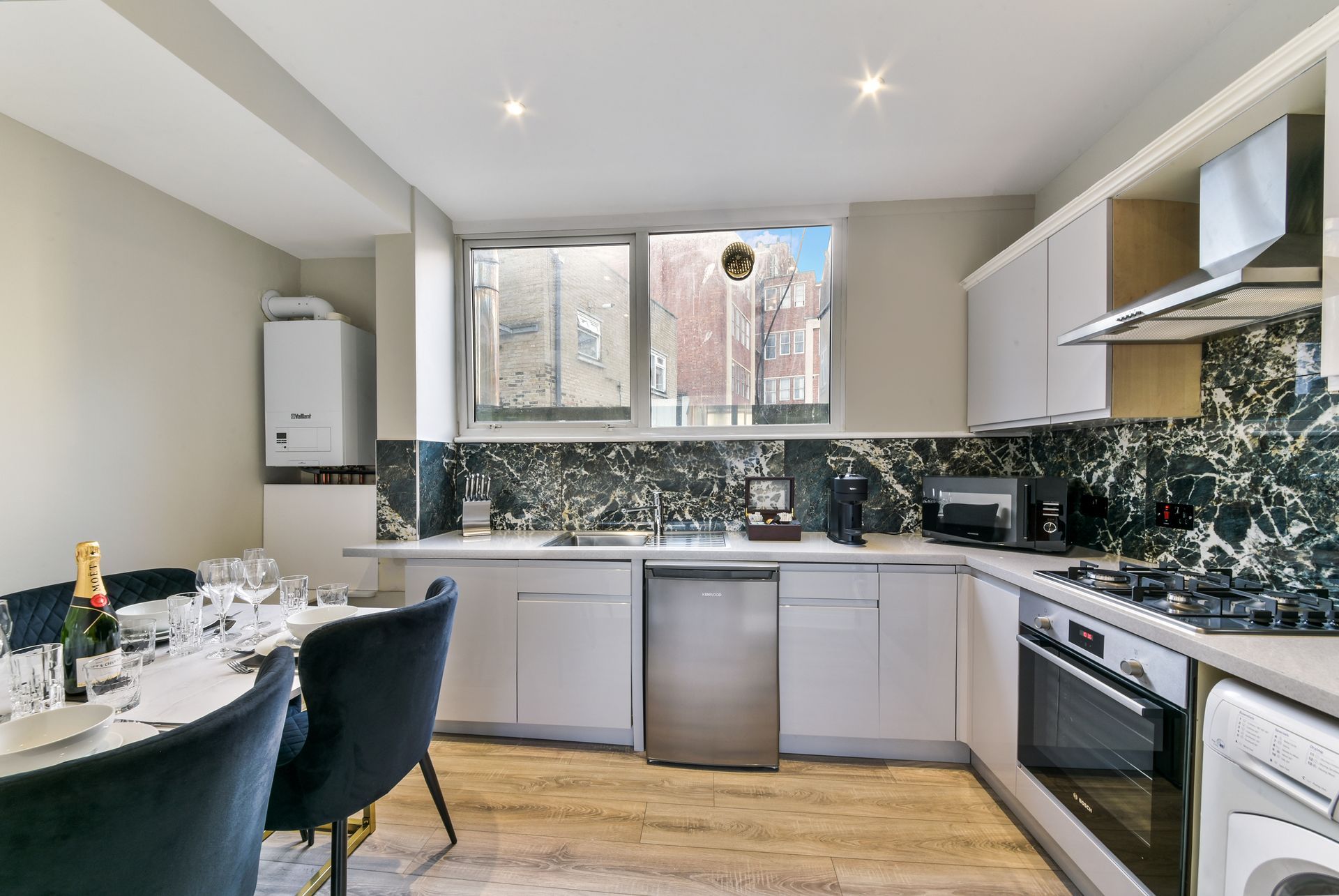 Modern kitchen with gray cabinets, patterned backsplash, stainless appliances, and a dining table by the window