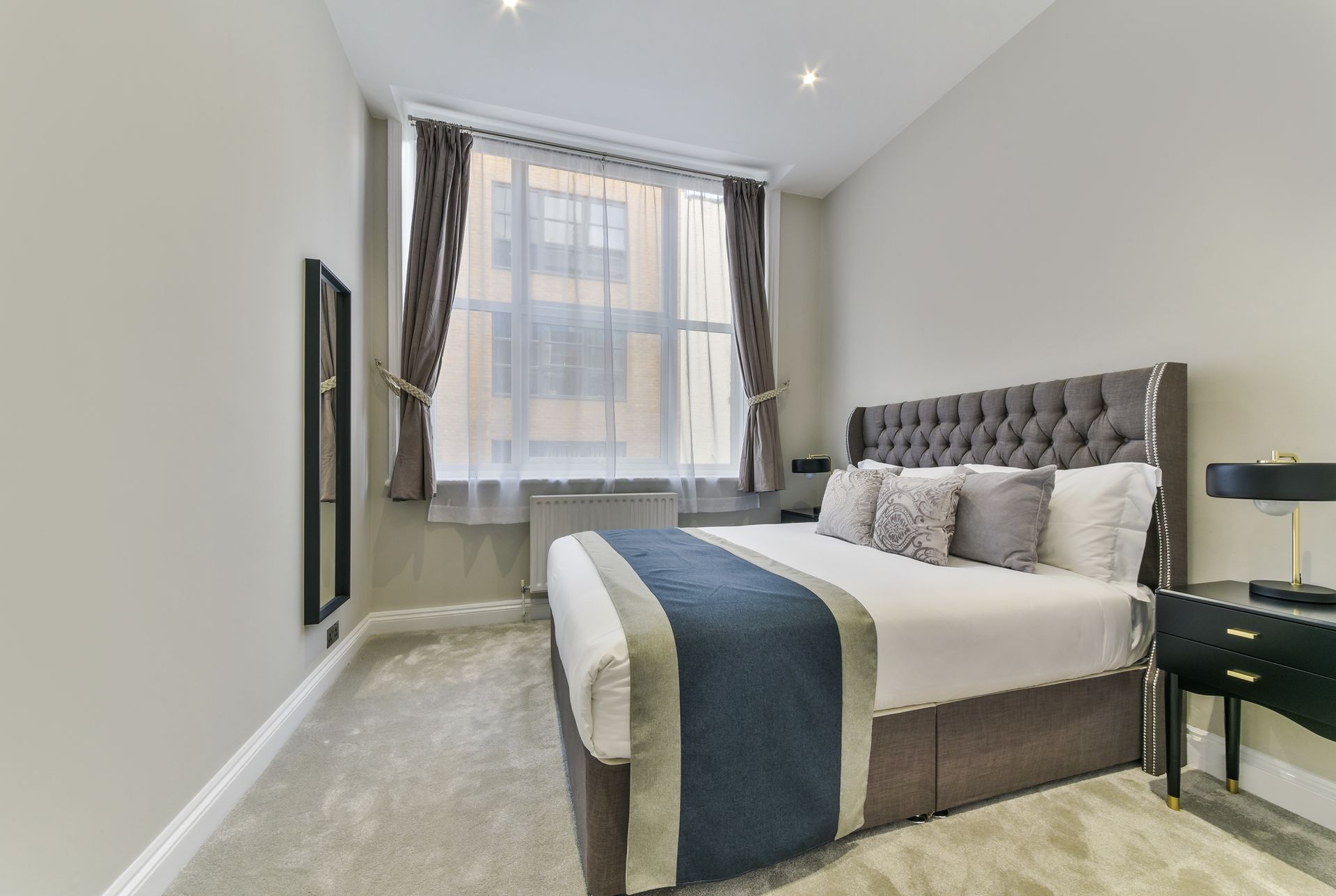 Modern bedroom with gray tufted bed, large window, and light carpet