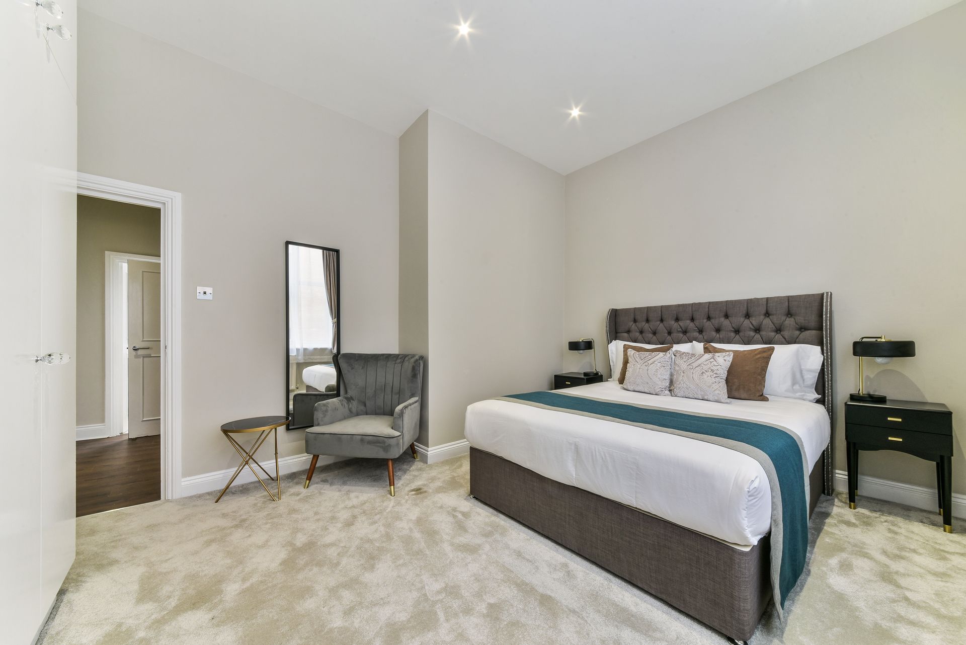 Bright bedroom with a tufted bed, mirrored chair, and neutral carpet walls