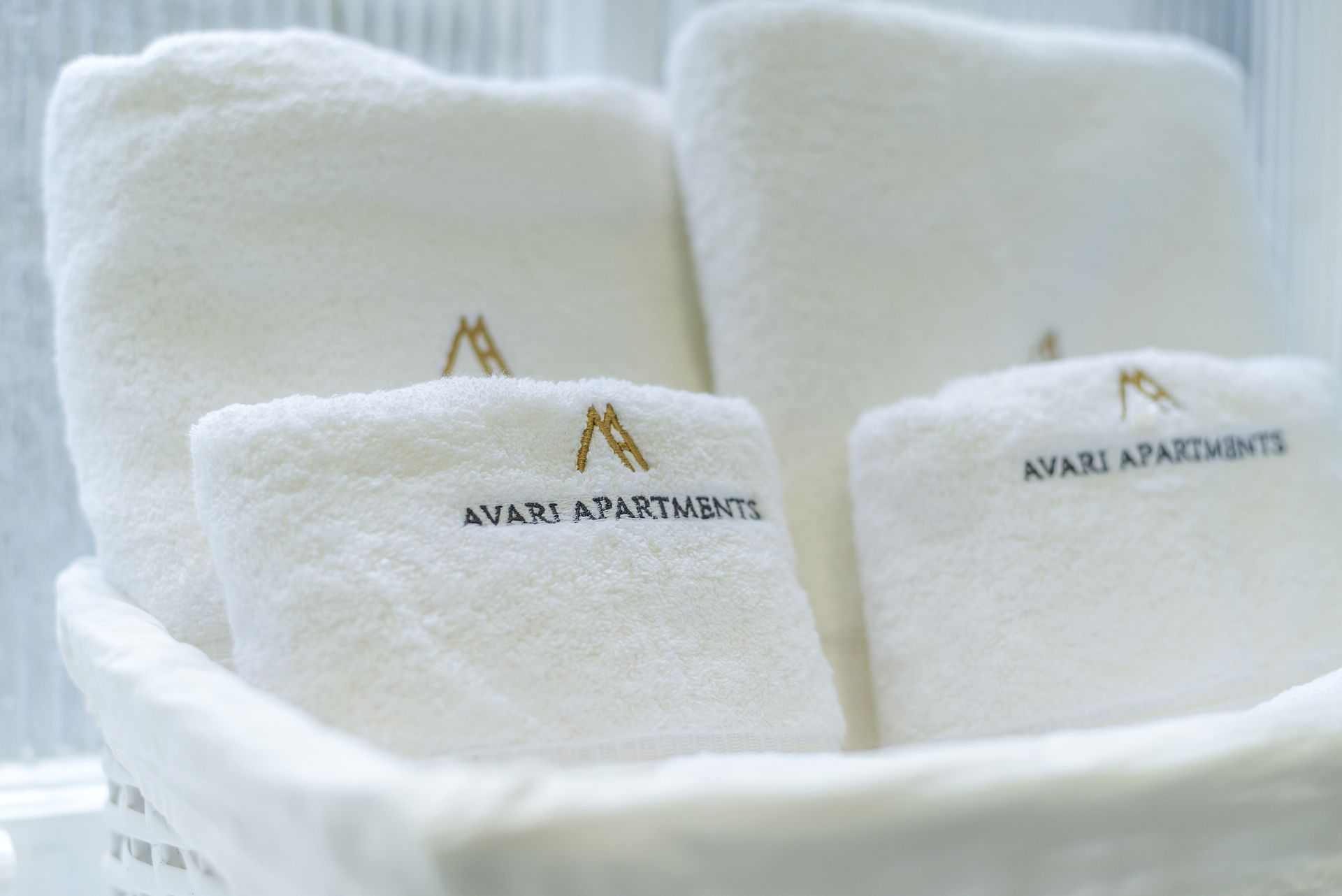 Folded white towels with gold logo in a spa basket, with a large towel in the background