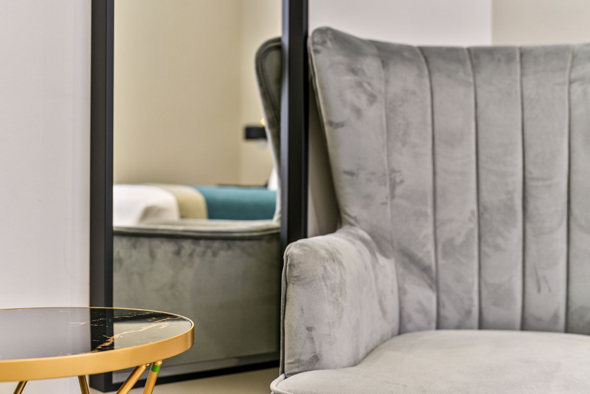 Gray upholstered chair beside a round glass coffee table with a gold base, reflected in a mirror.