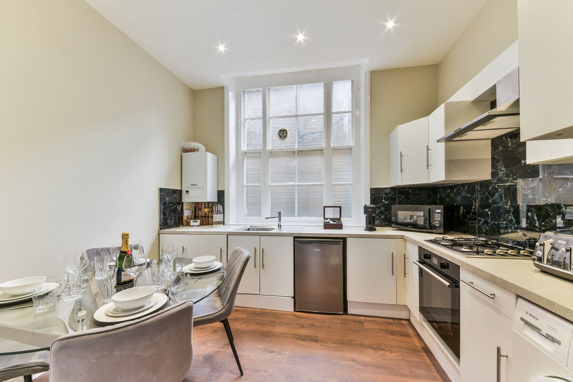 Bright modern kitchen with white cabinets, black backsplash, and a small dining table by a window