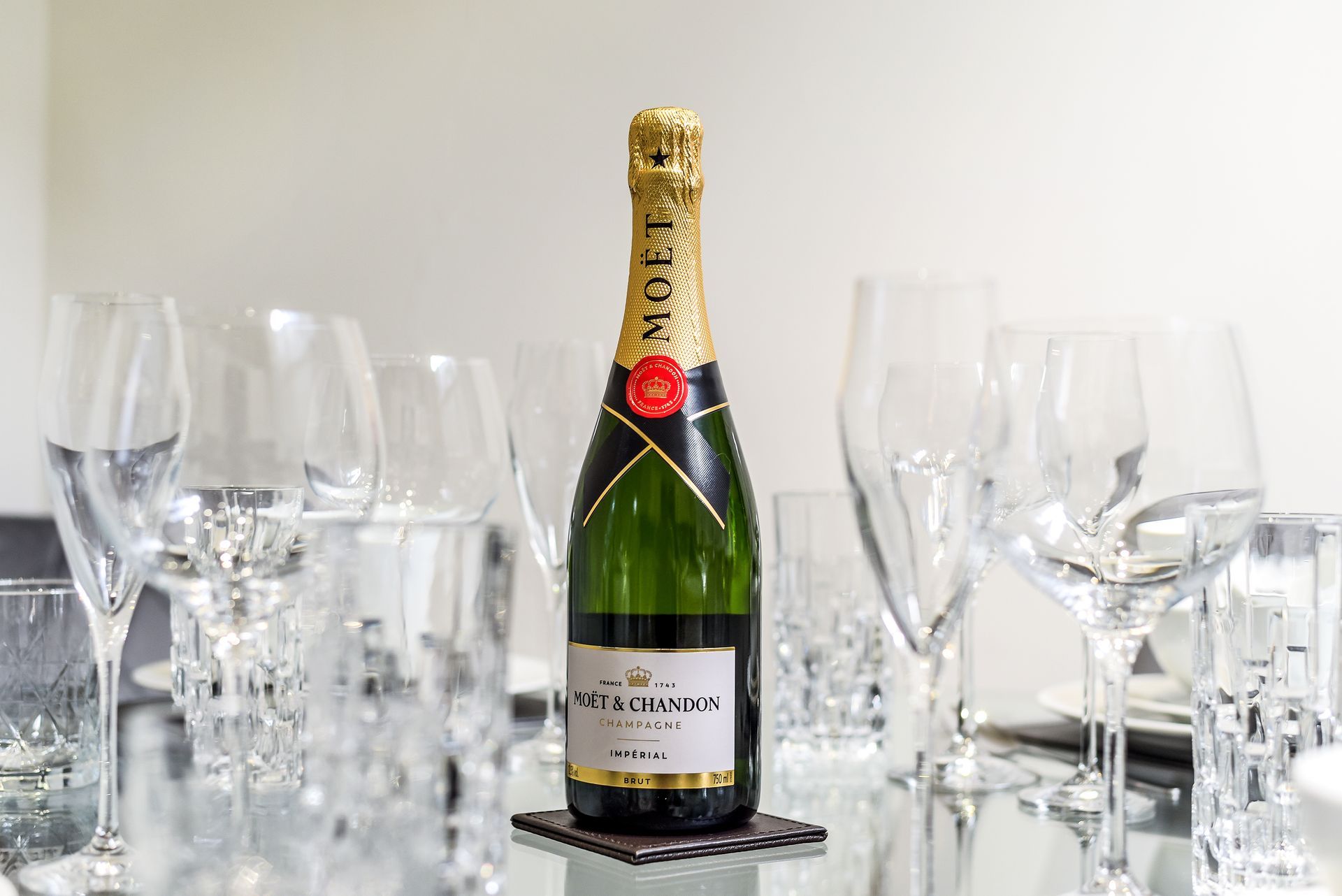 Champagne bottle on a mirrored table surrounded by empty wine glasses