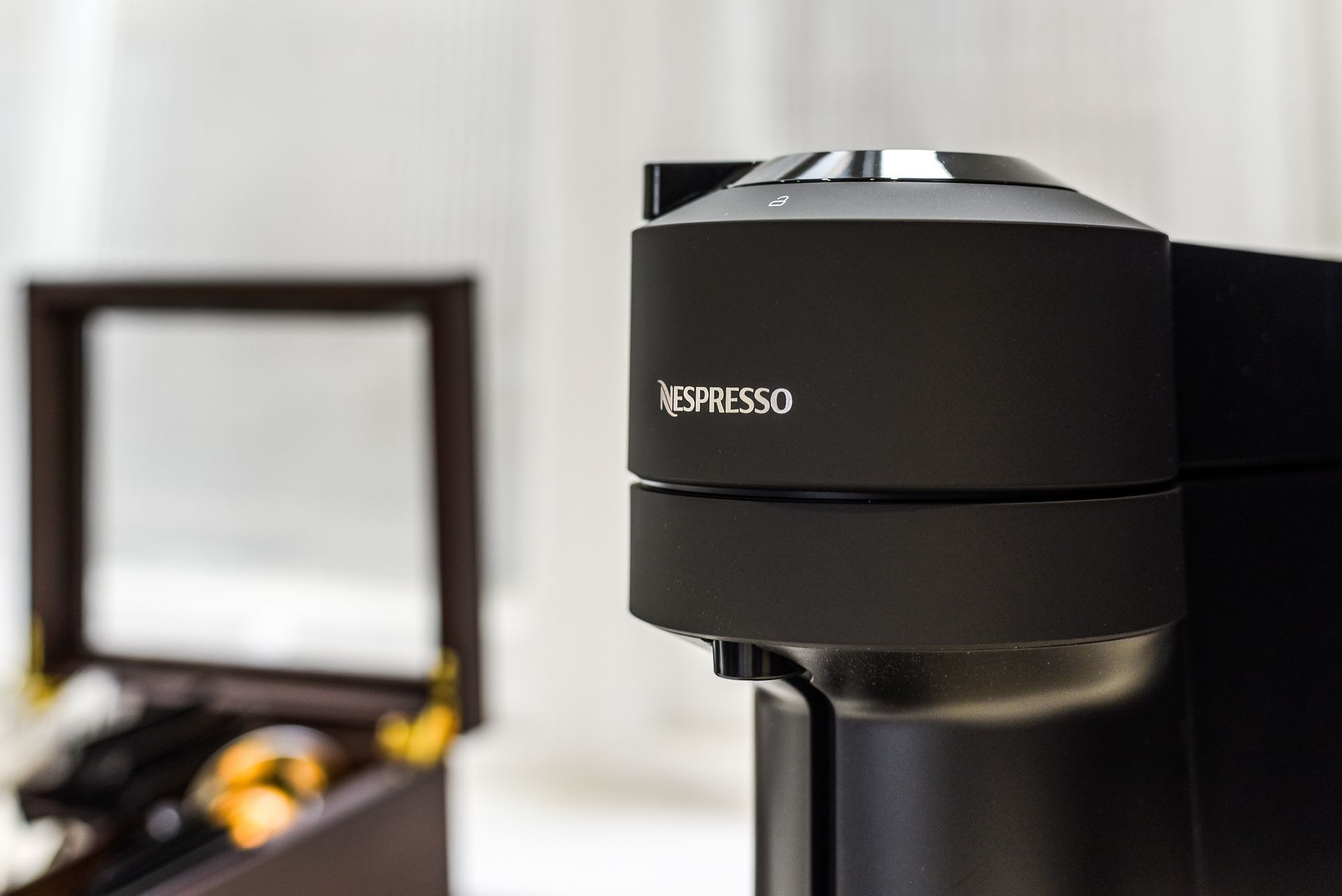 Black Nespresso coffee machine on a counter, with an open case blurred in the background