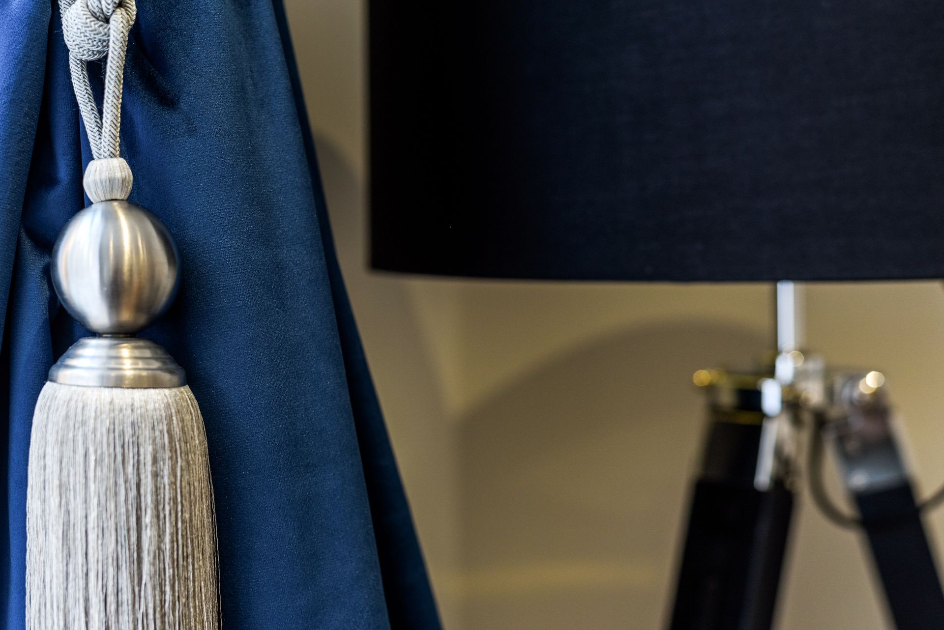 Blue curtain tieback with silver tassel beside a black table lamp on a stand