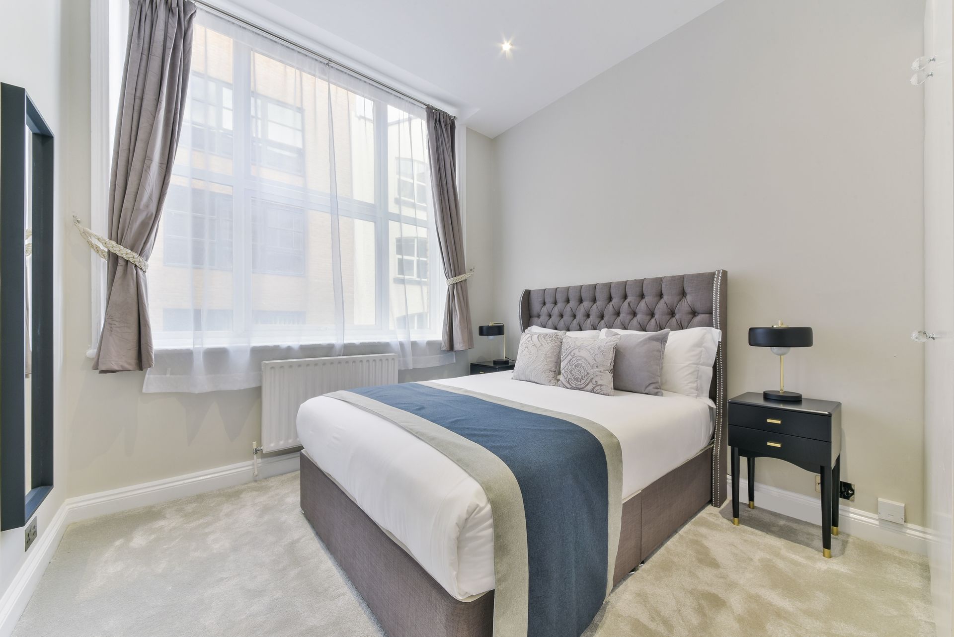 Bright bedroom with a bed, large window, and light gray decor