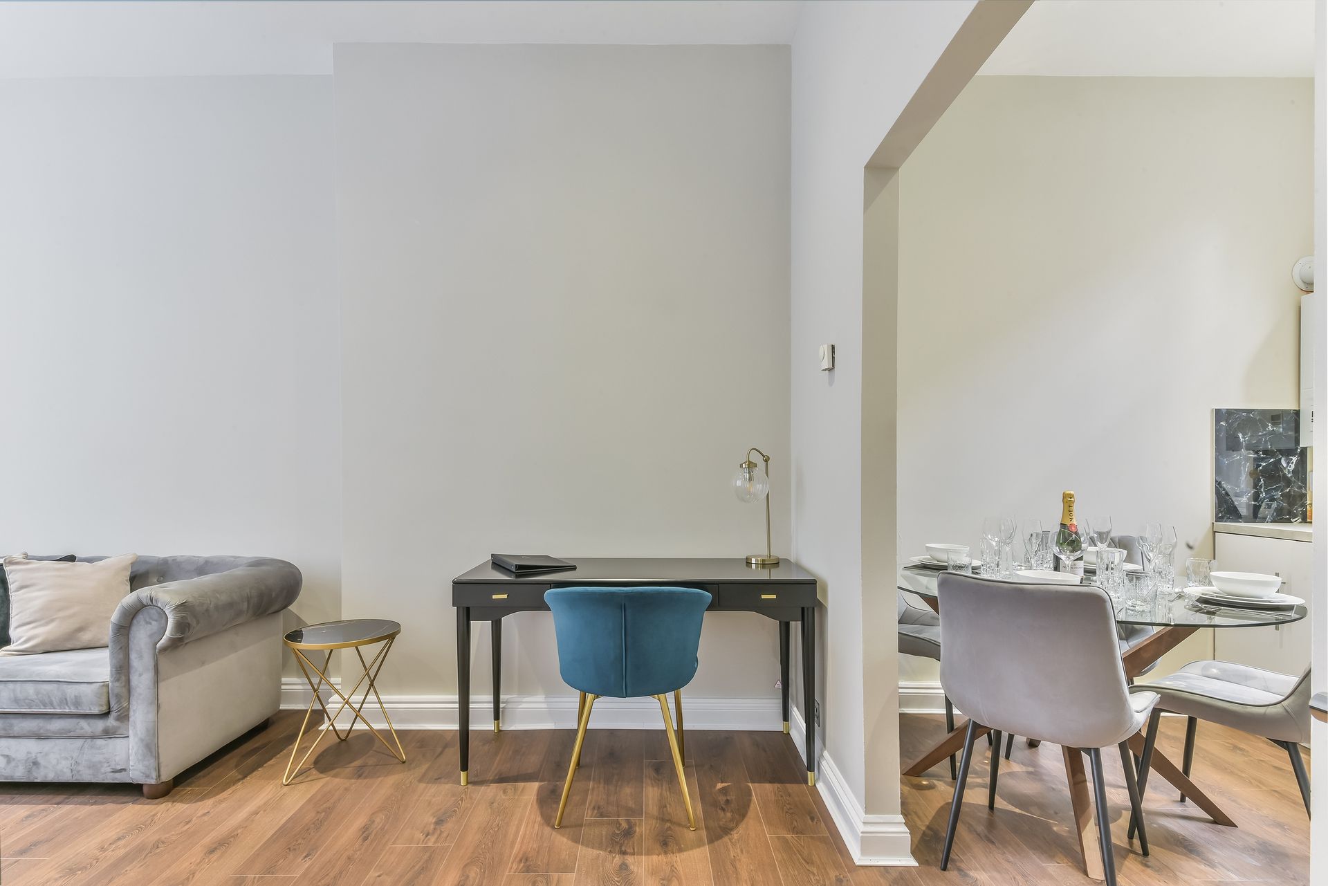 Bright living space with gray sofa, desk and blue chair, opening to a dining area with white table and chairs