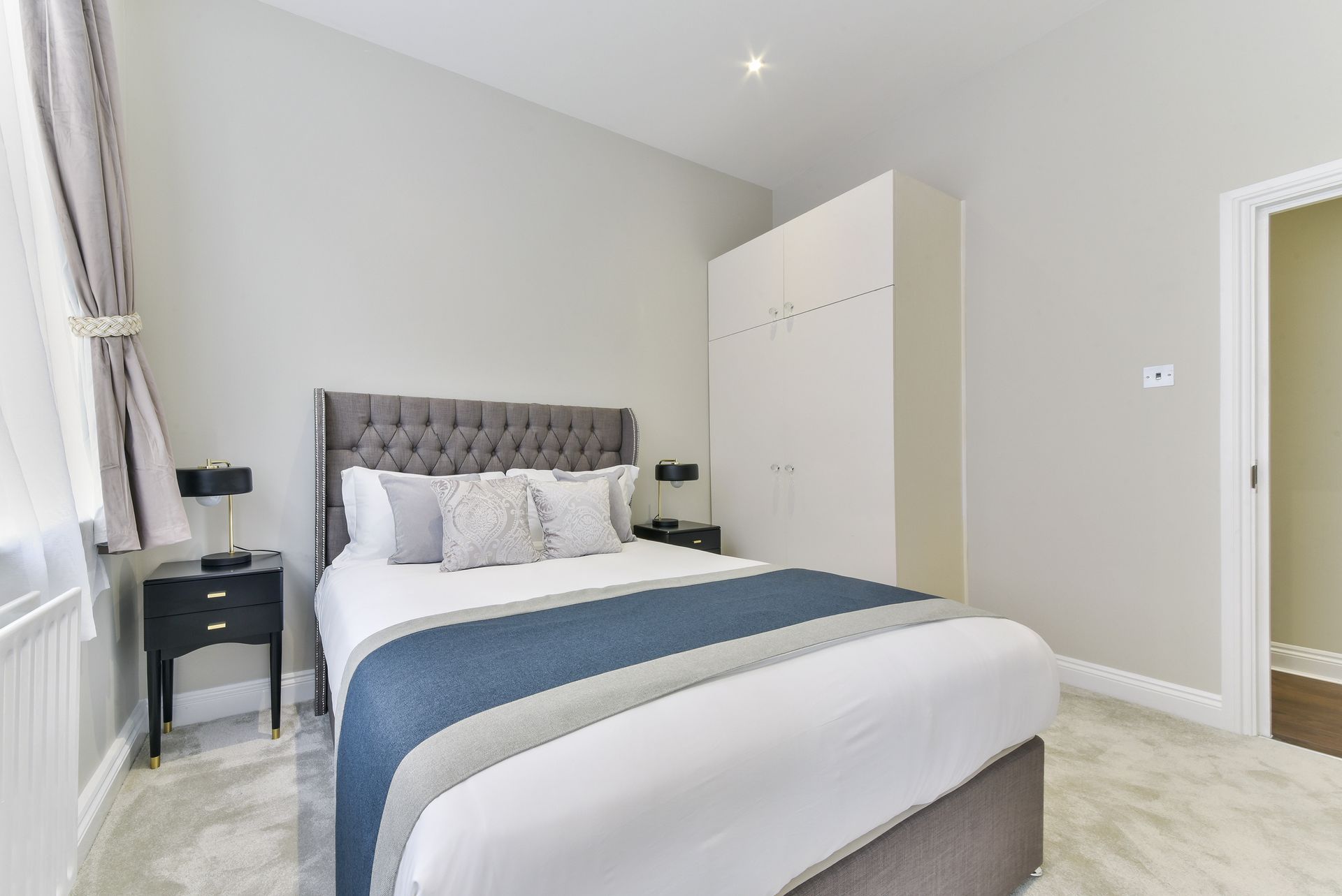 Bright modern bedroom with a neatly made bed, gray headboard, white wardrobe, and bedside table