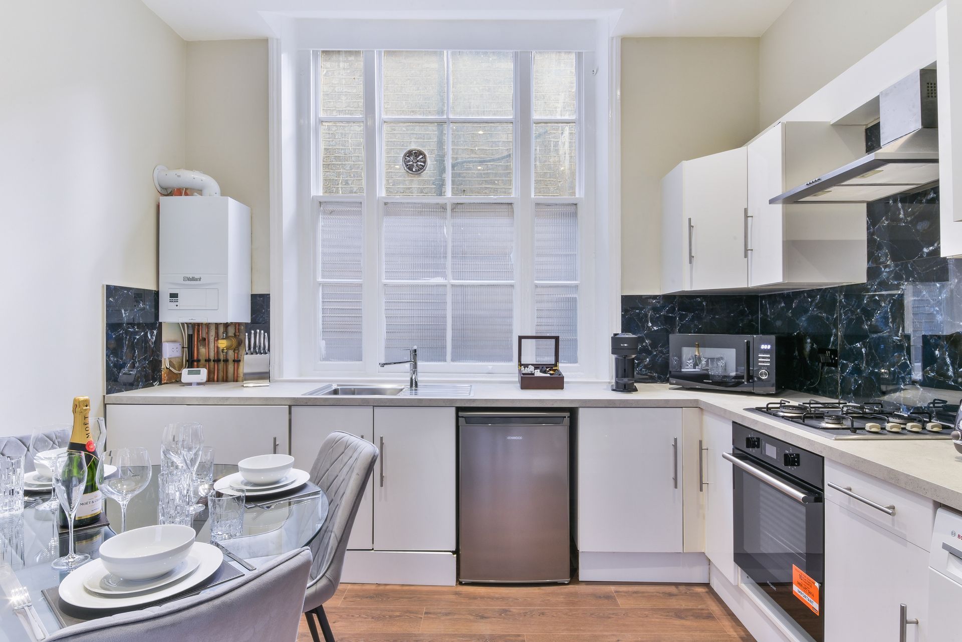 Bright modern kitchen with white cabinets, window, dining table, and stainless steel appliances