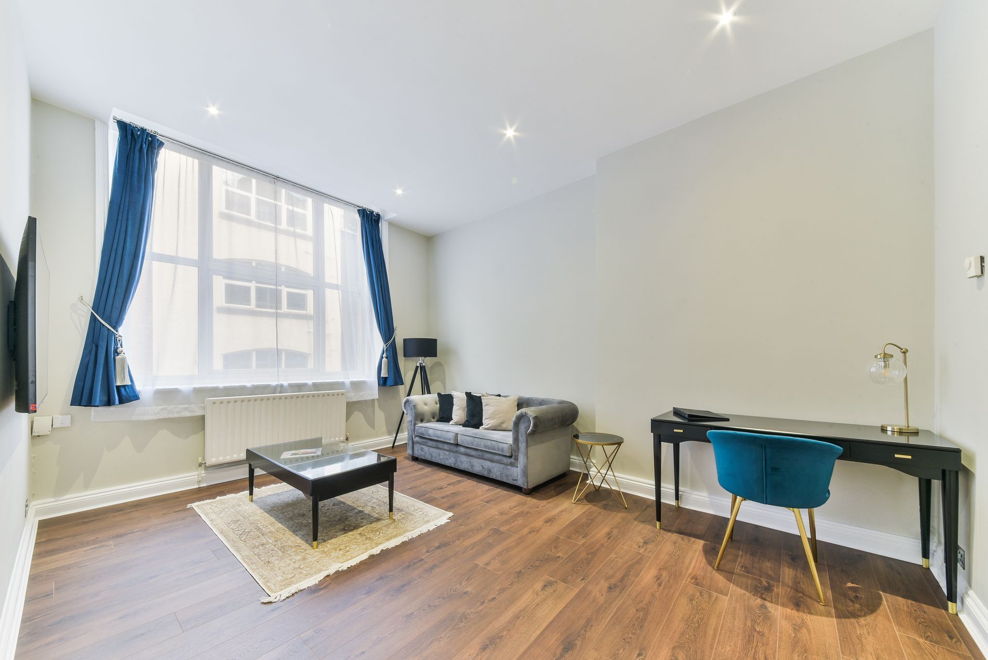 Bright modern living room with sofa, desk, coffee table, and blue curtains by a large window.
