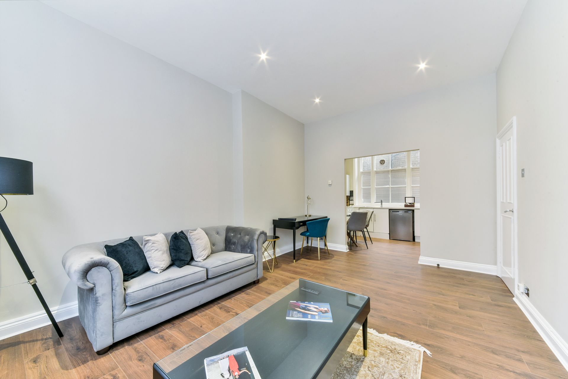 Bright living room with gray sofa, black coffee table, and small desk by an open kitchen pass-through.