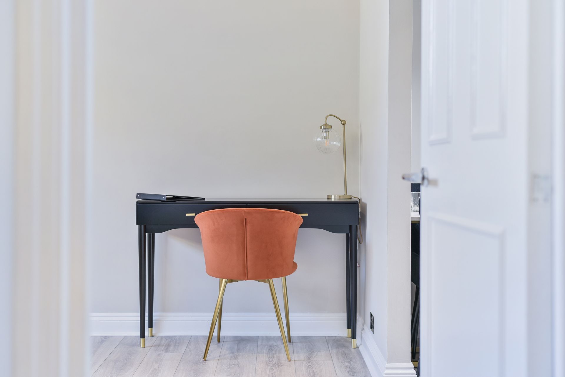 Minimalist home office with black desk and orange chair in a bright white room