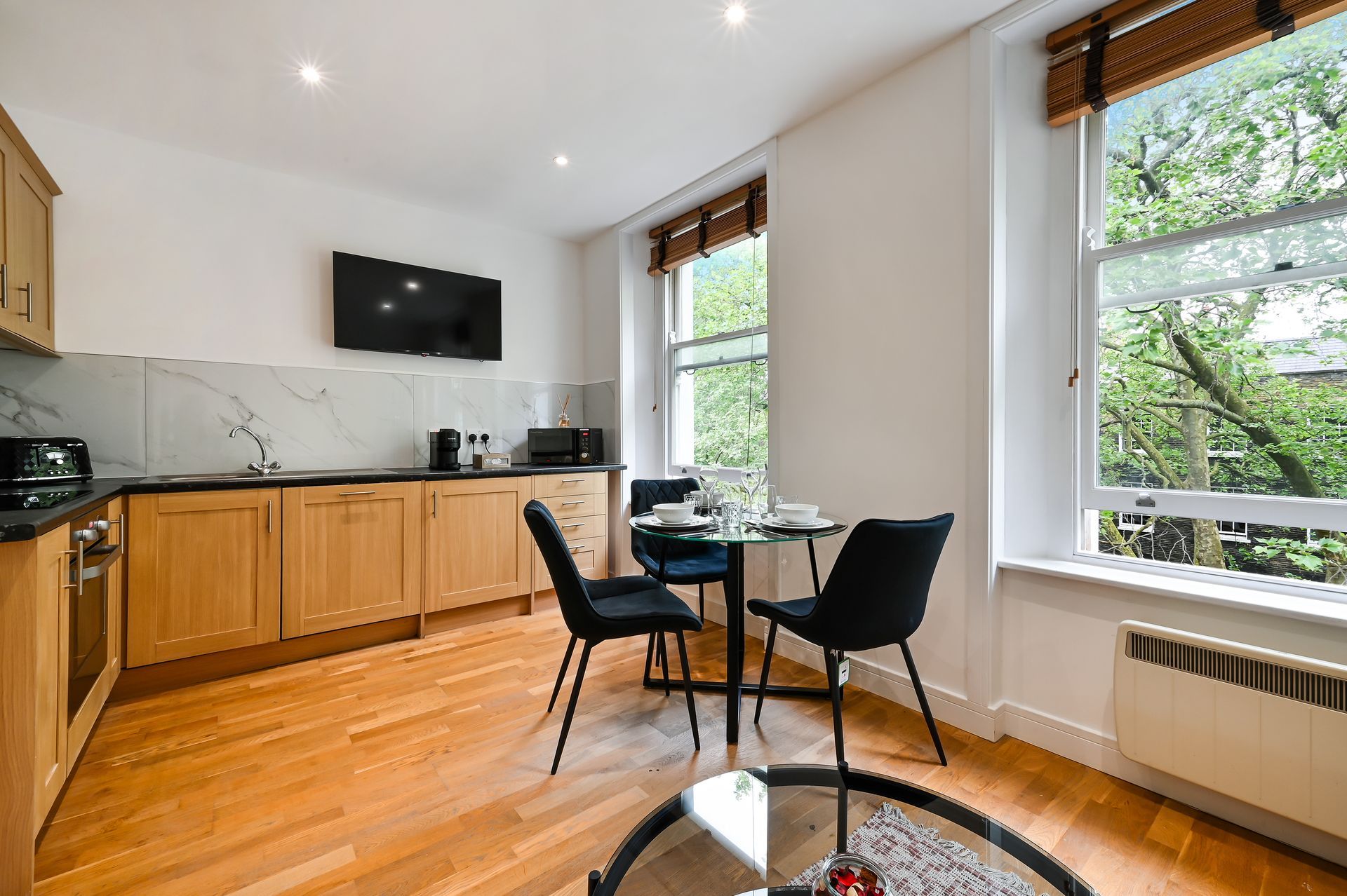 Bright modern kitchen with wood cabinets, black dining chairs, and large windows.